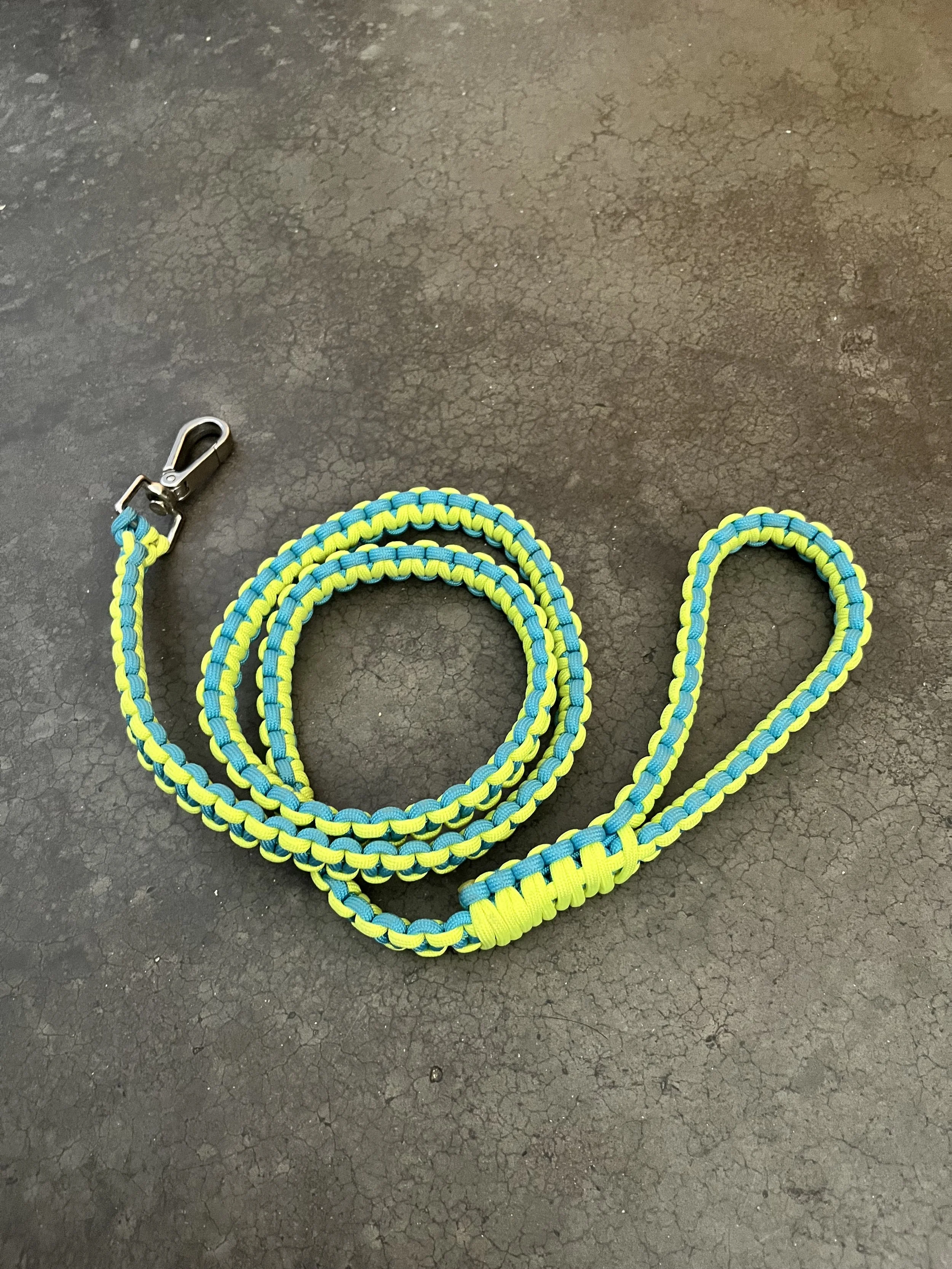 Colorful braided leash with metal clip resting on cracked black floor.