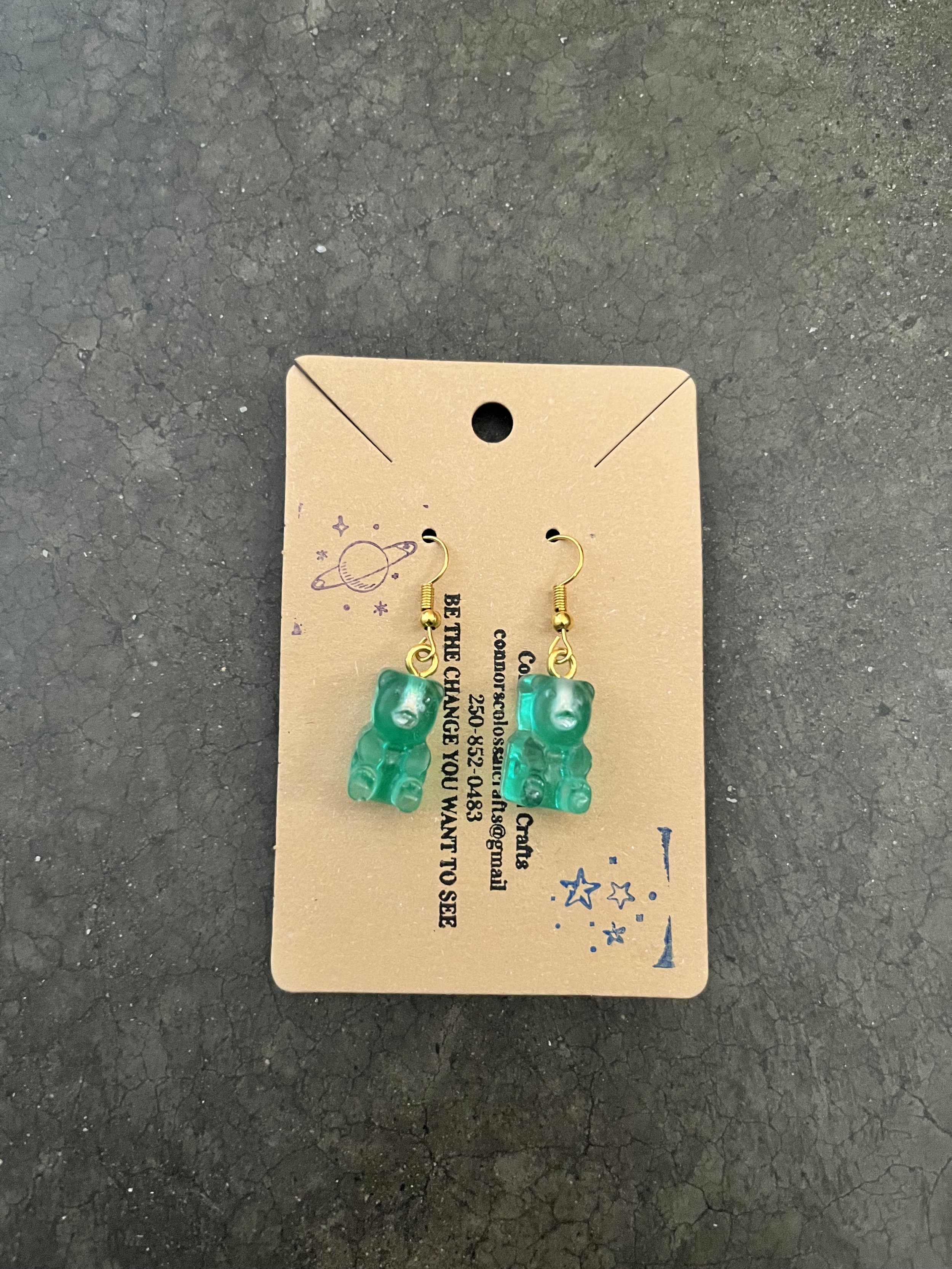 Green gummy bear earrings on tan cardboard display.