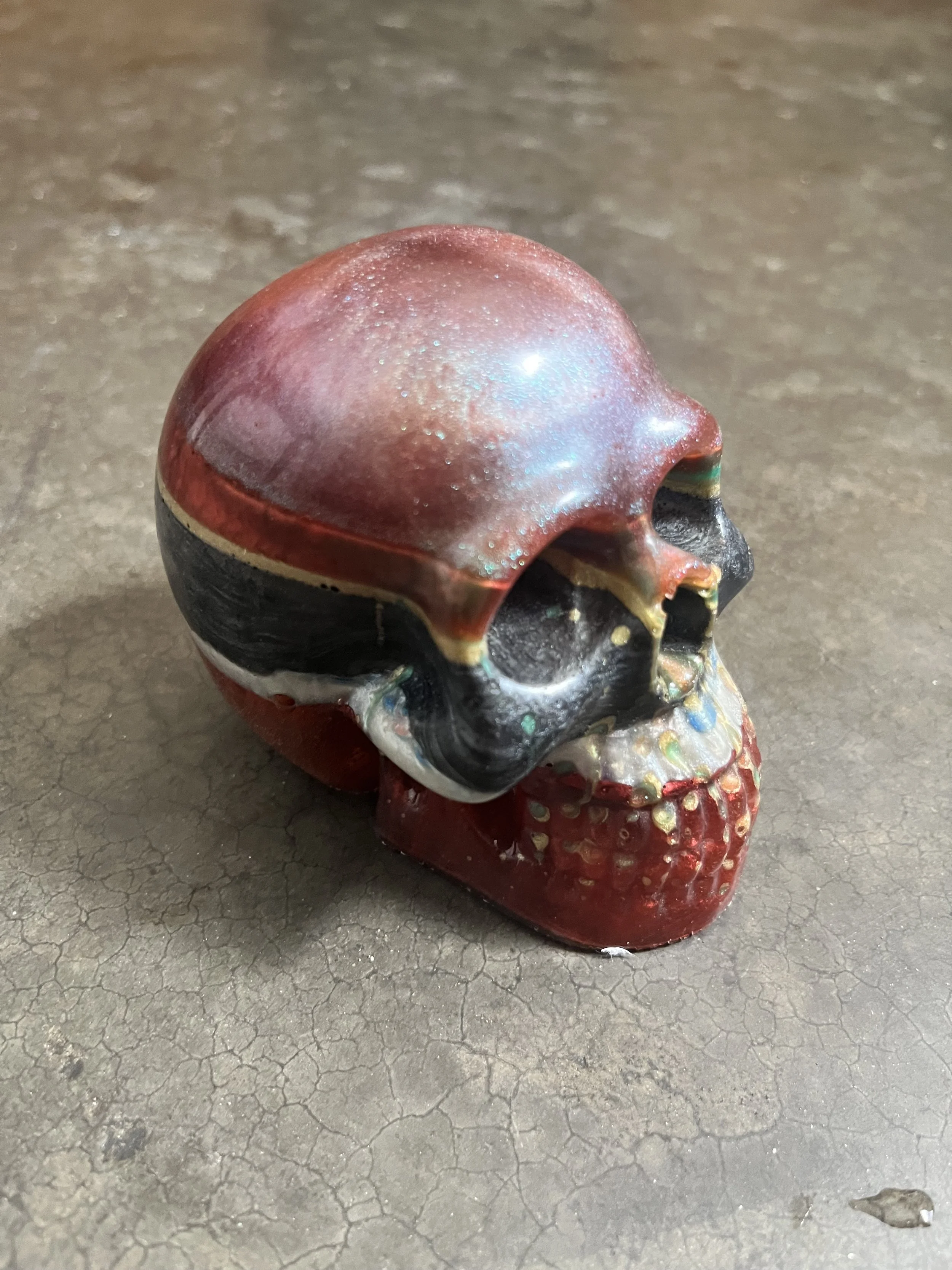 Colorful skull-shaped epoxy resin object on cracked gray floor.