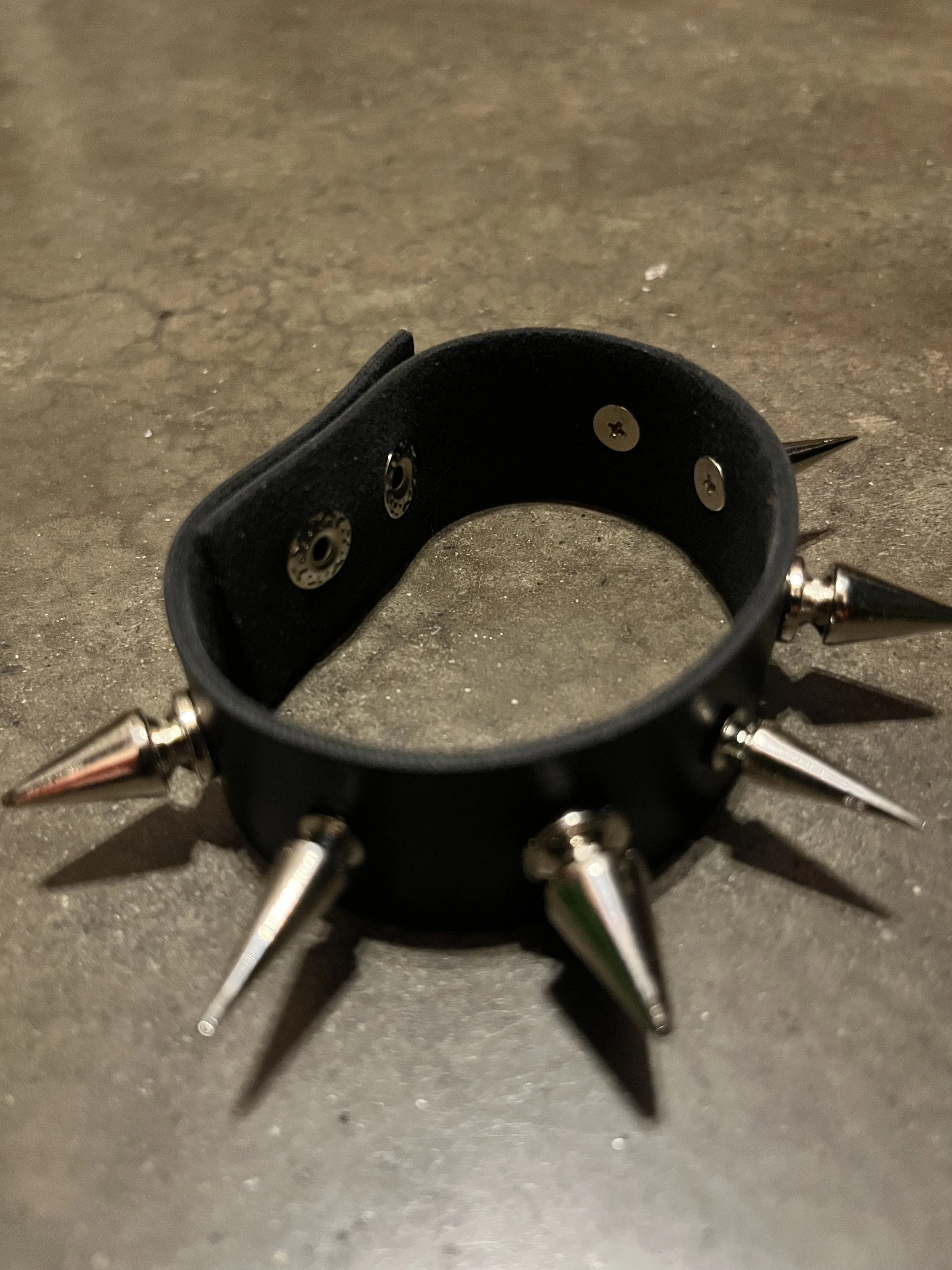 Close-up of a black leather collar with metal spikes on a gray surface.