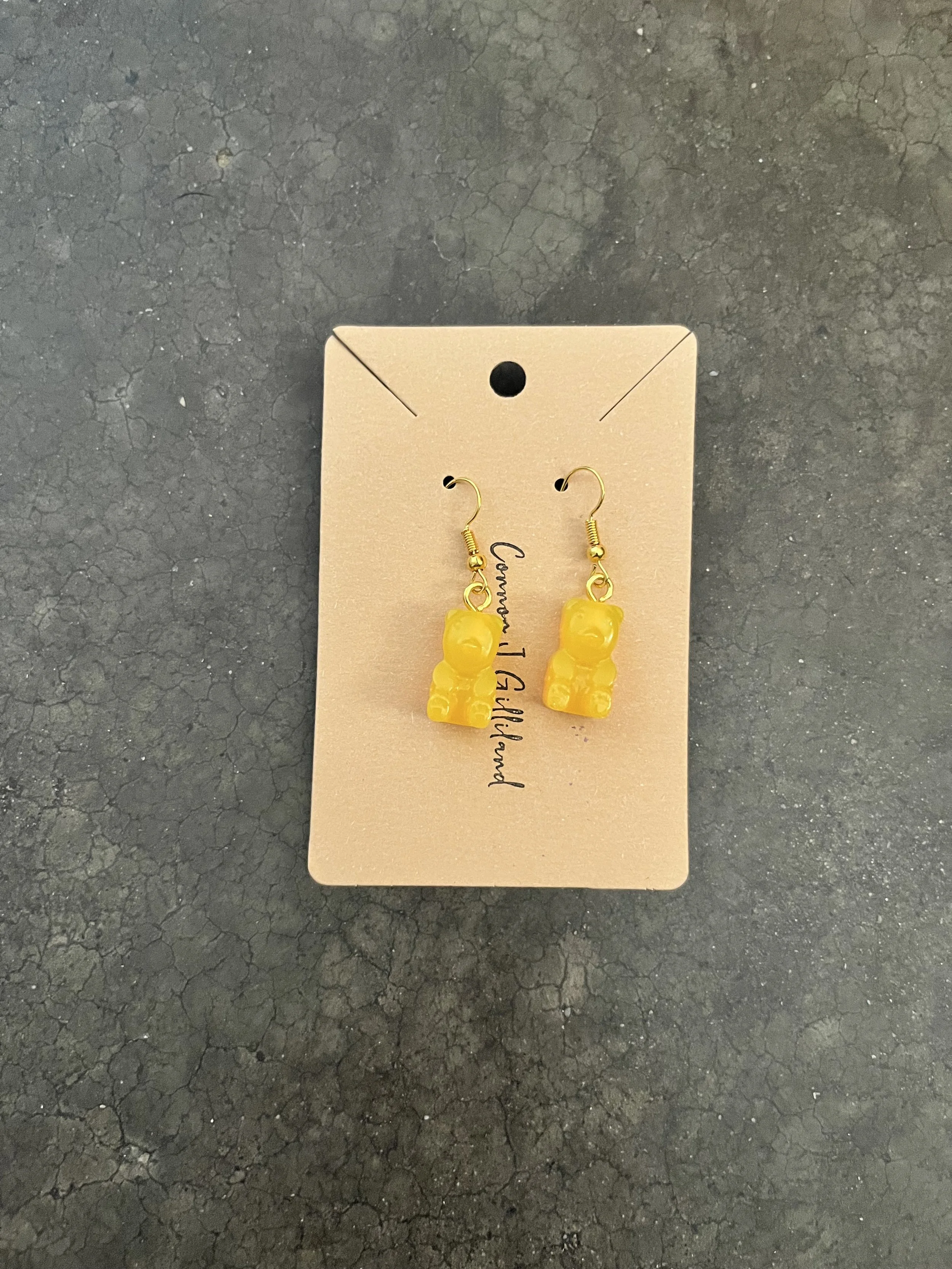 Yellow epoxy resin earrings  hanging on a beige display card, placed on a black cracked surface.