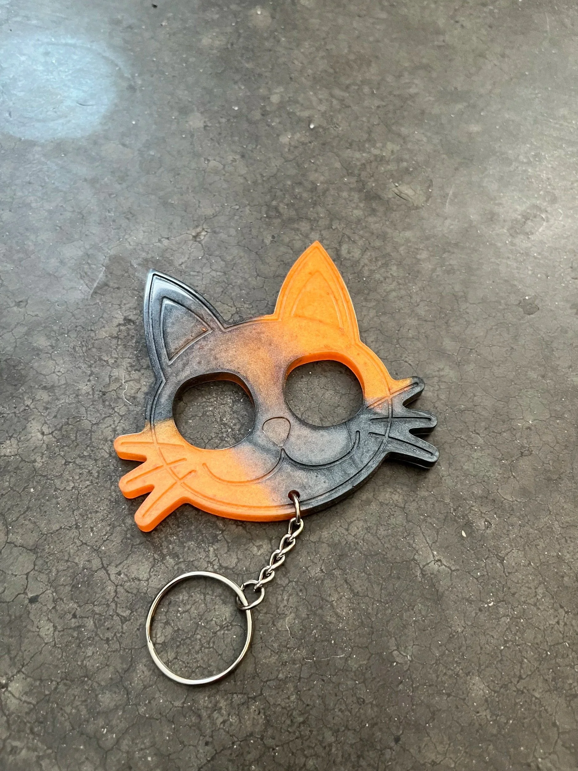 A handmade orange and black cat shaped resin epoxy emergency keychain.