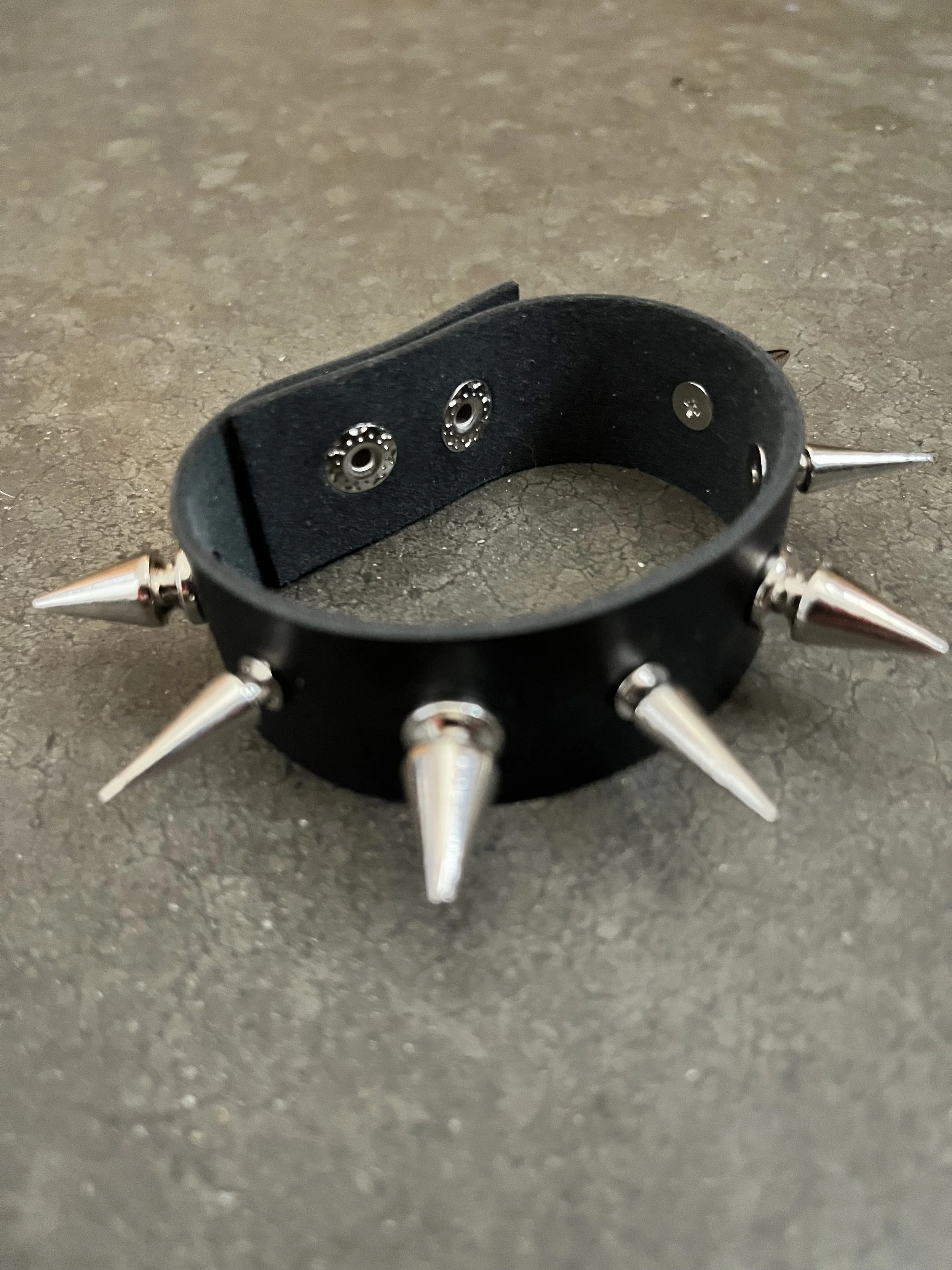 Black leather wrist cuff with metallic spike attachments on a gray surface.