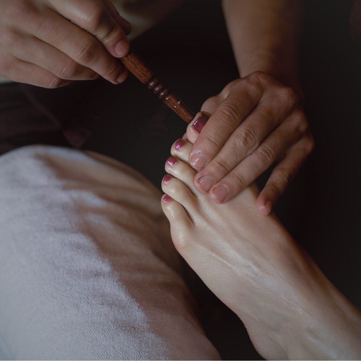 A person receiving a foot massage from a massage therapist using a wooden massage tool.