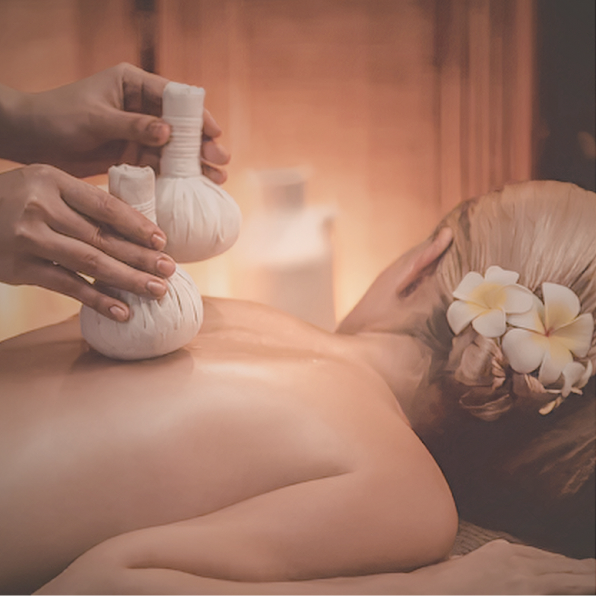 Person receiving a massage with herbal compress balls in a spa setting, decorated with flowers.