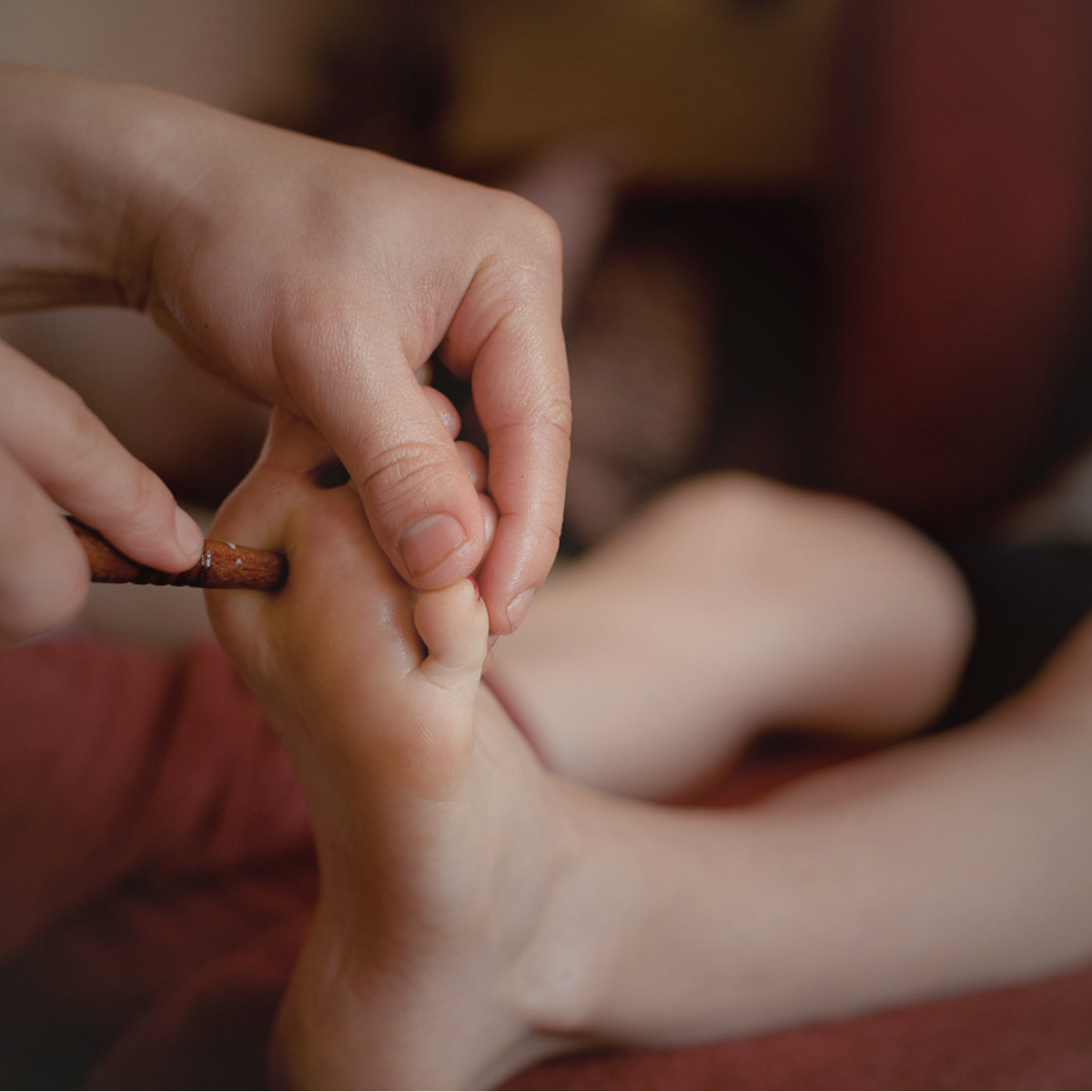 Close-up of a person holding a small stick and gently massaging a child's foot.