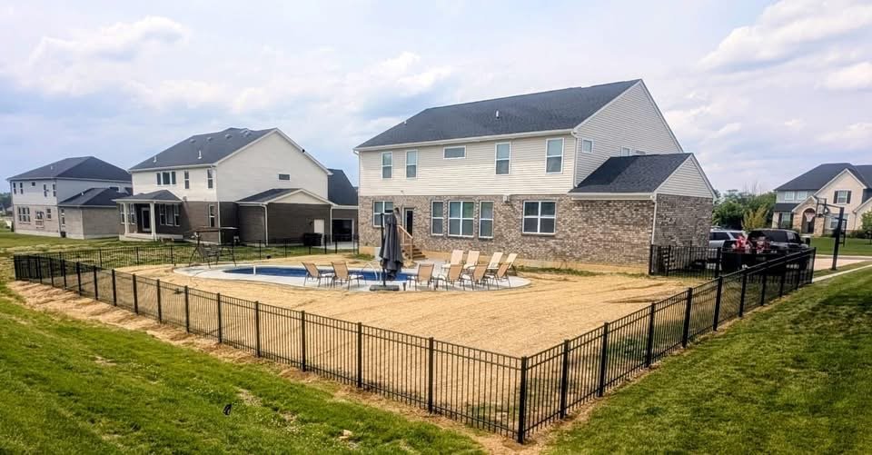 Backyard with a swimming pool, lounge chairs, and a patio umbrella, surrounded by a black metal fence, with neighboring houses in the background.