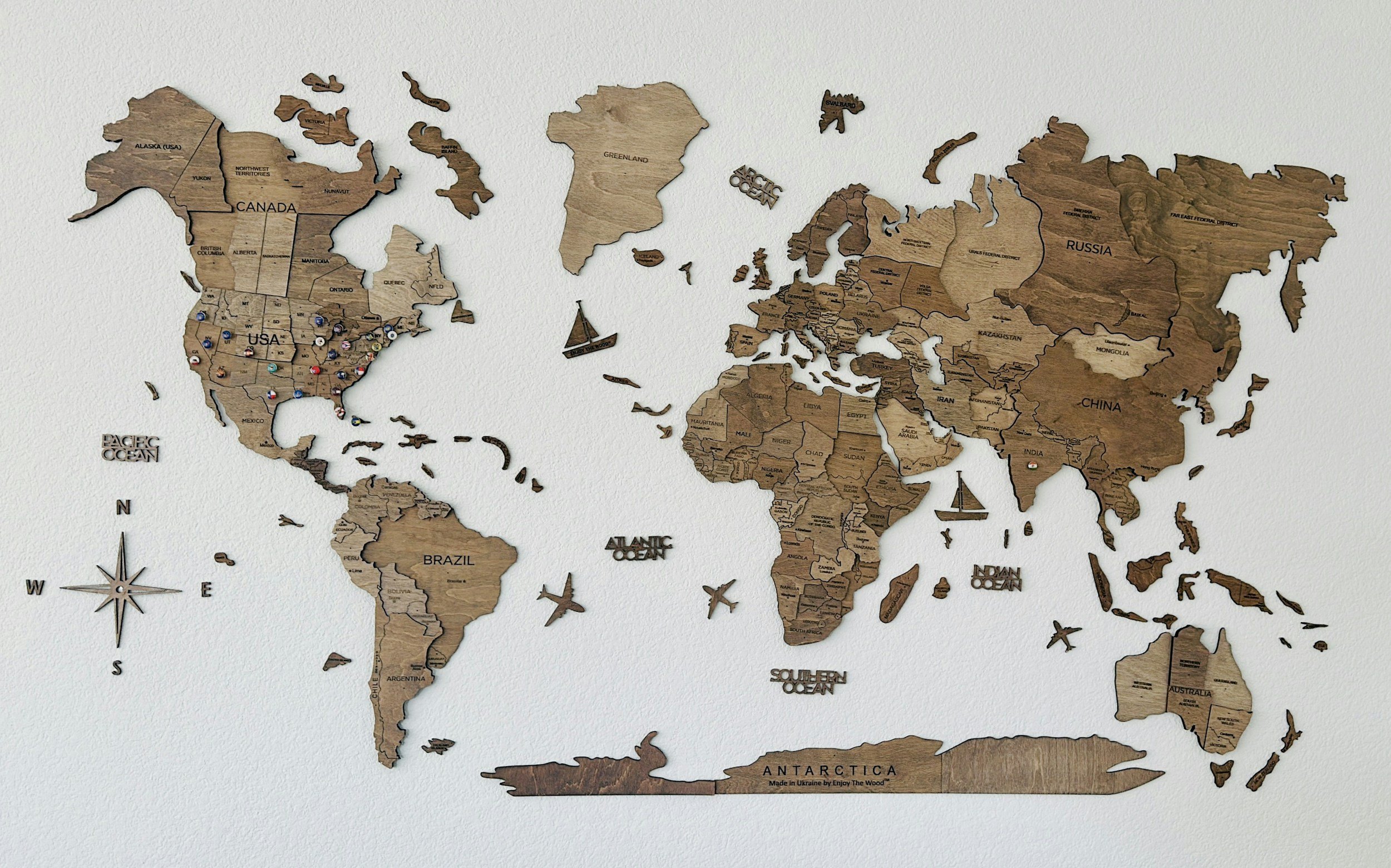 Wooden world map on wall with country names and regional labels.