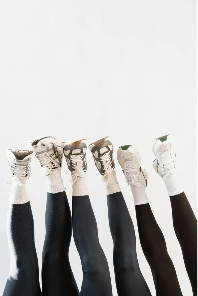 Six people with legs raised, wearing athletic shoes and leggings, against a white background.