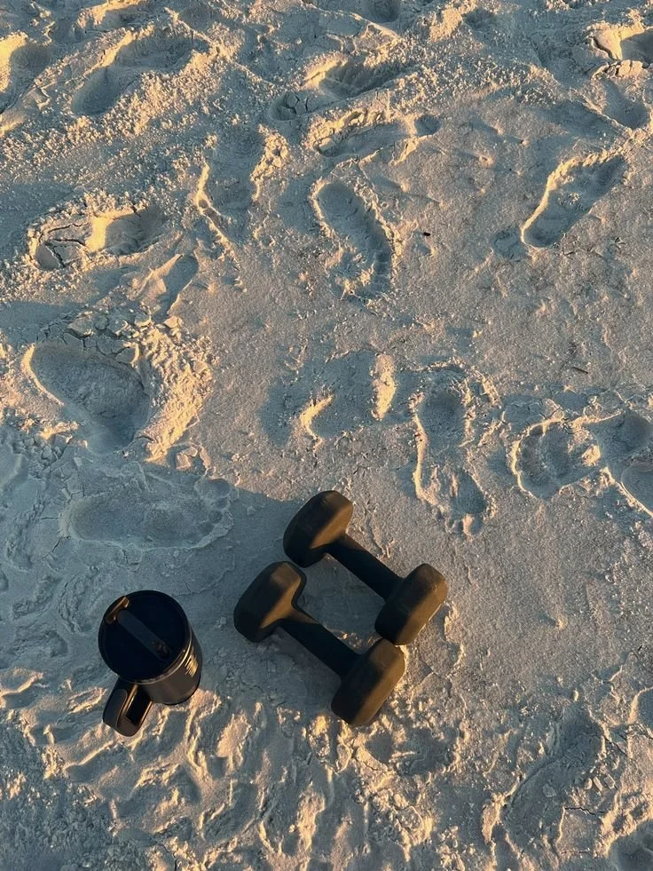 An outdoor scene with footprints in the snow, a black tumbler, and a pair of black dumbbells.
