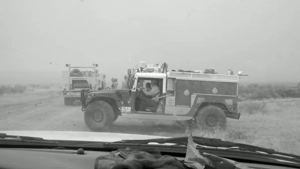 A convoy of fire trucks traveling down a dirt road viewed from inside a vehicle.