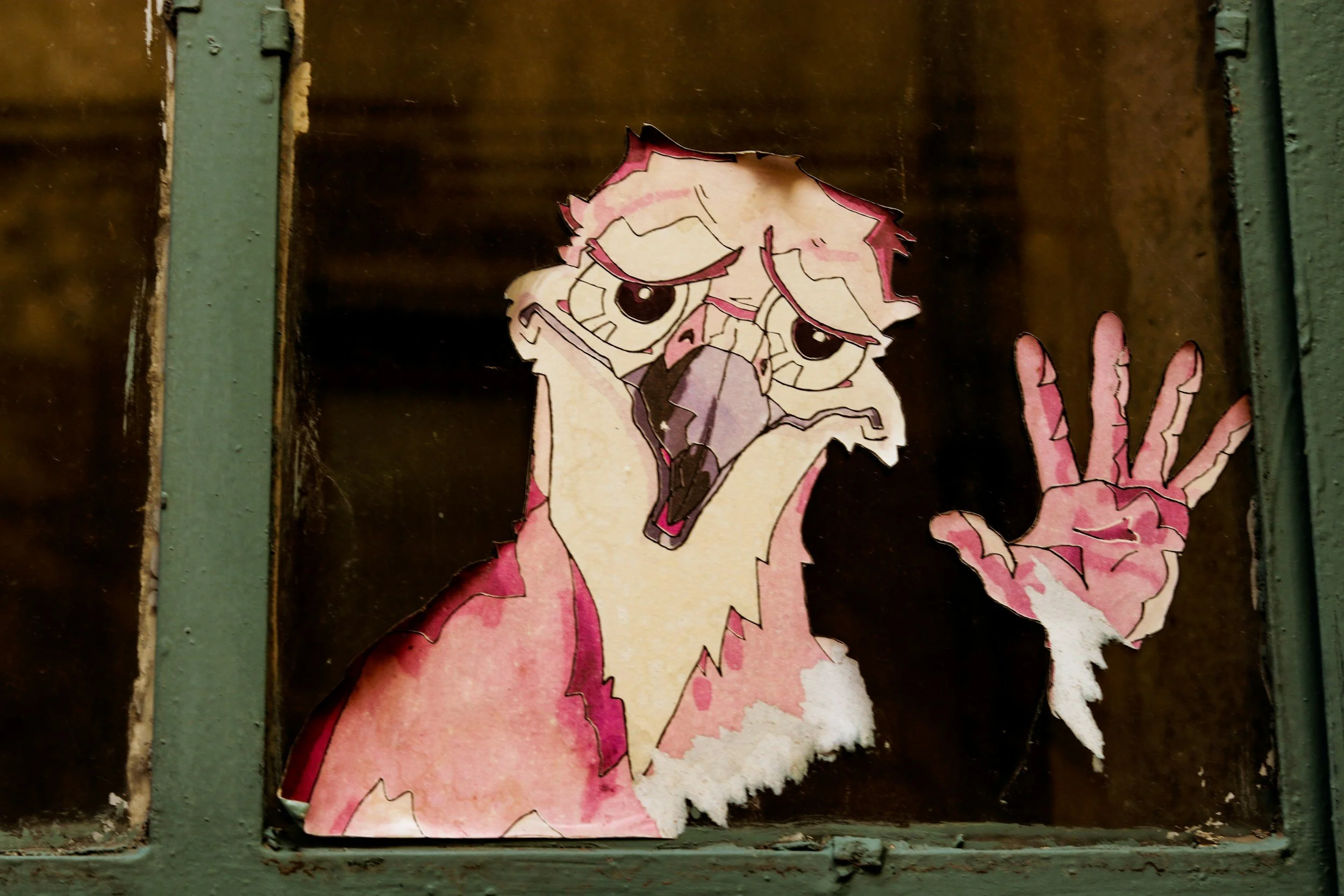 Street art sticker of a pink dragon with large eyes and sharp teeth on a weathered wooden surface, partially torn.