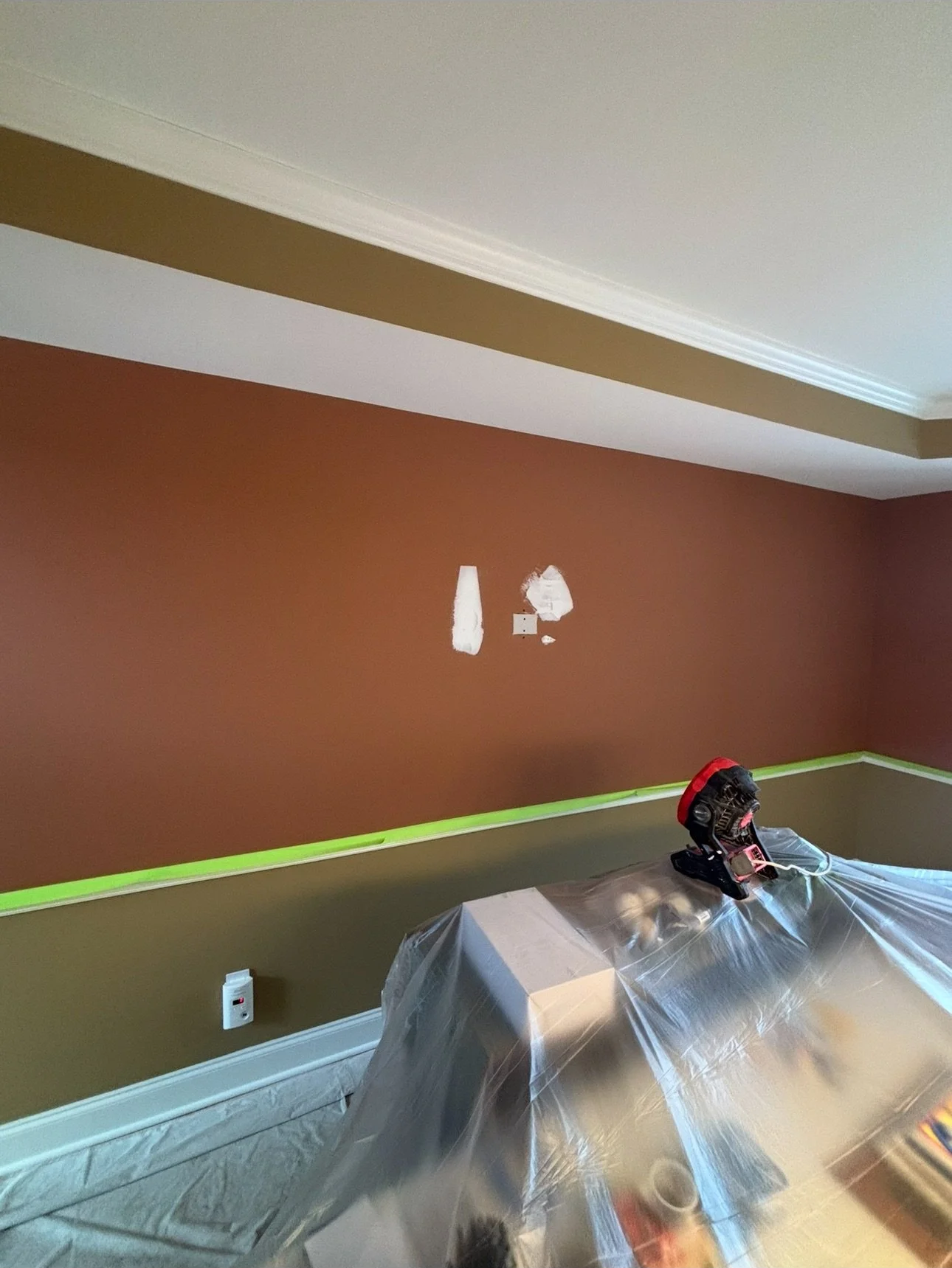 a two-color interior room gets fresh paint inside of a home with personal belongings covered with plastic