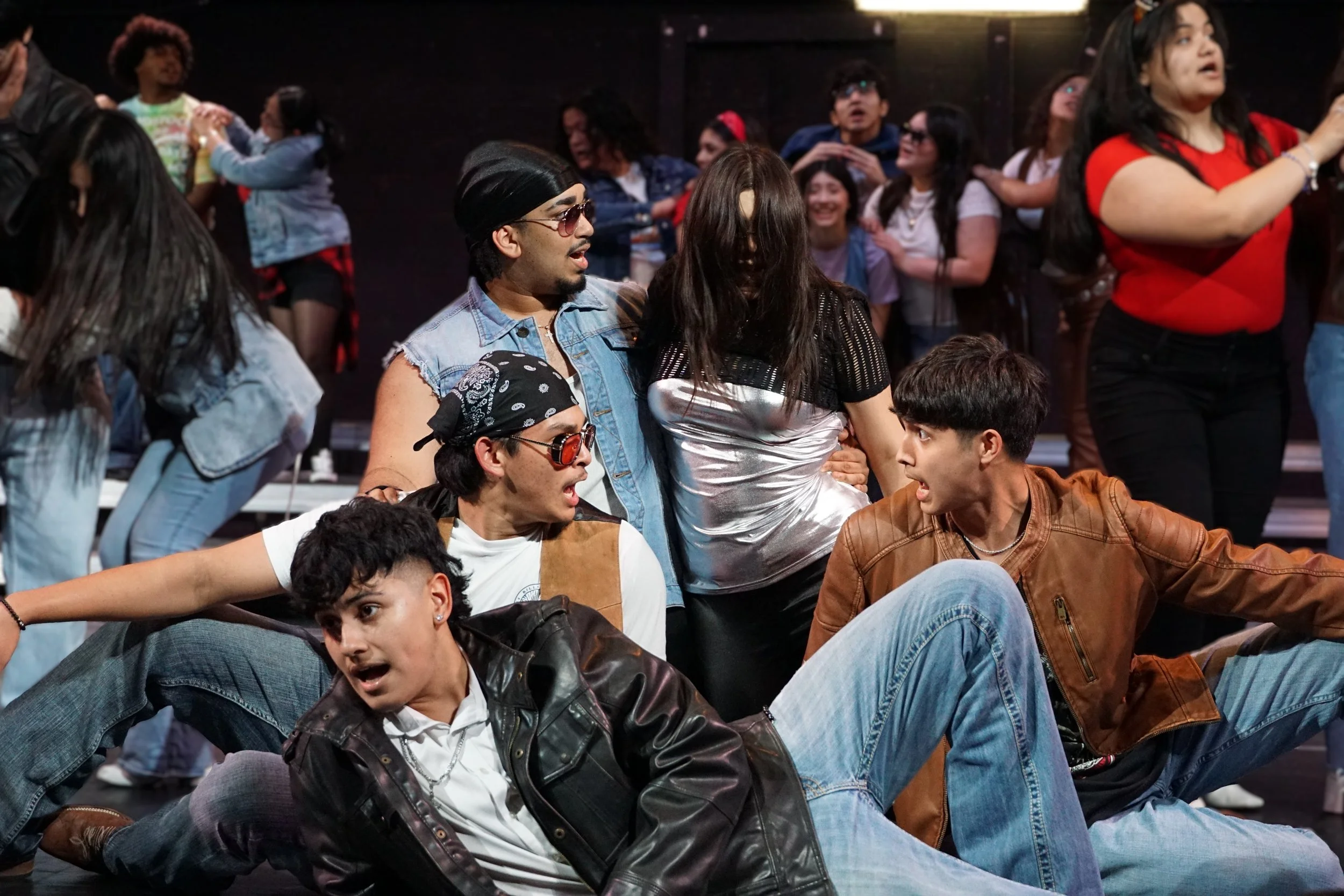 Group of young people dancing and socializing at a party or club, with some seated on the floor and others standing in the background.