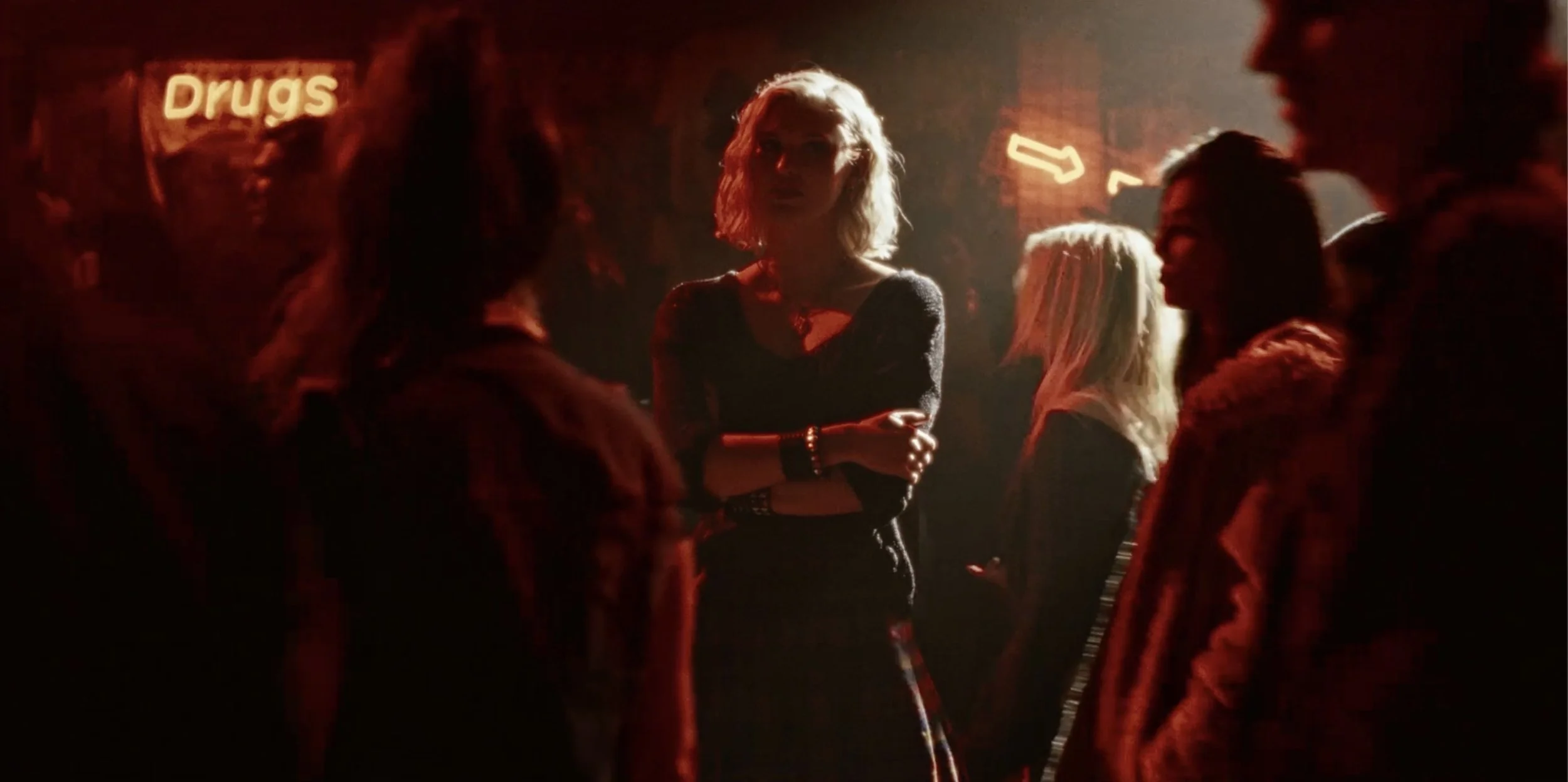 Woman stands in a club with a neon-lit Drugs sign