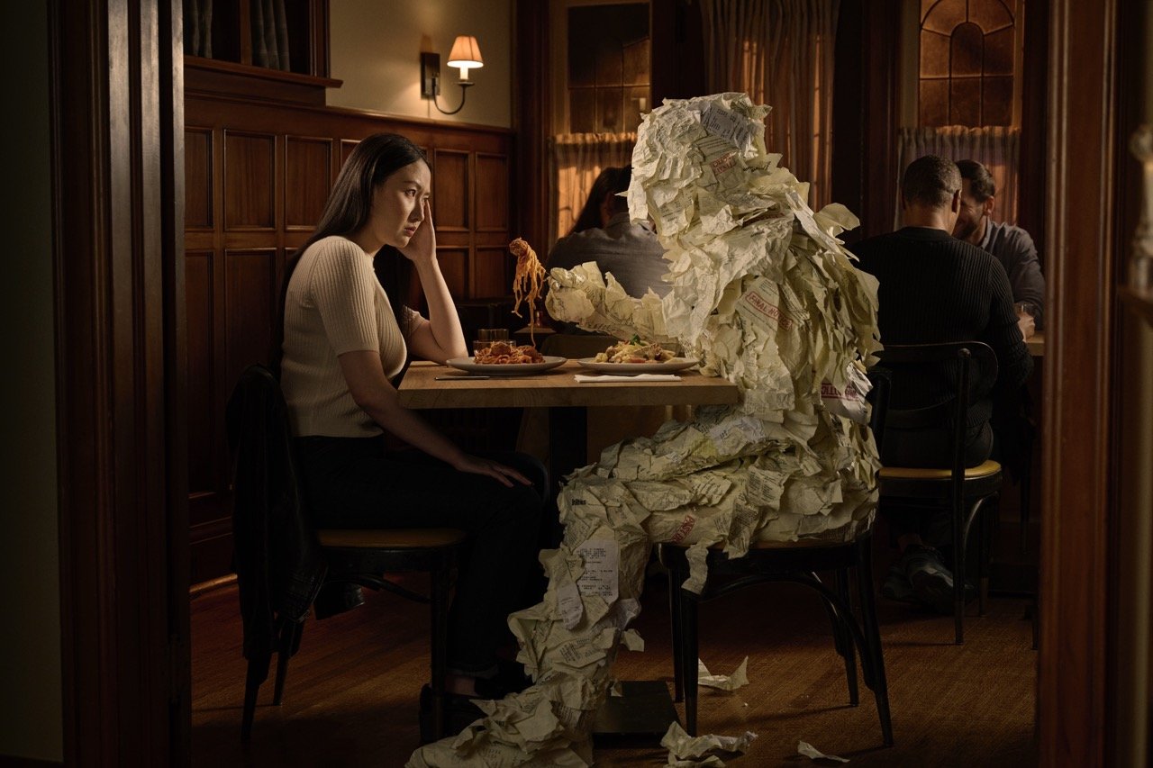 Dissatisfied woman dining with a person covered 100% in bills etc.