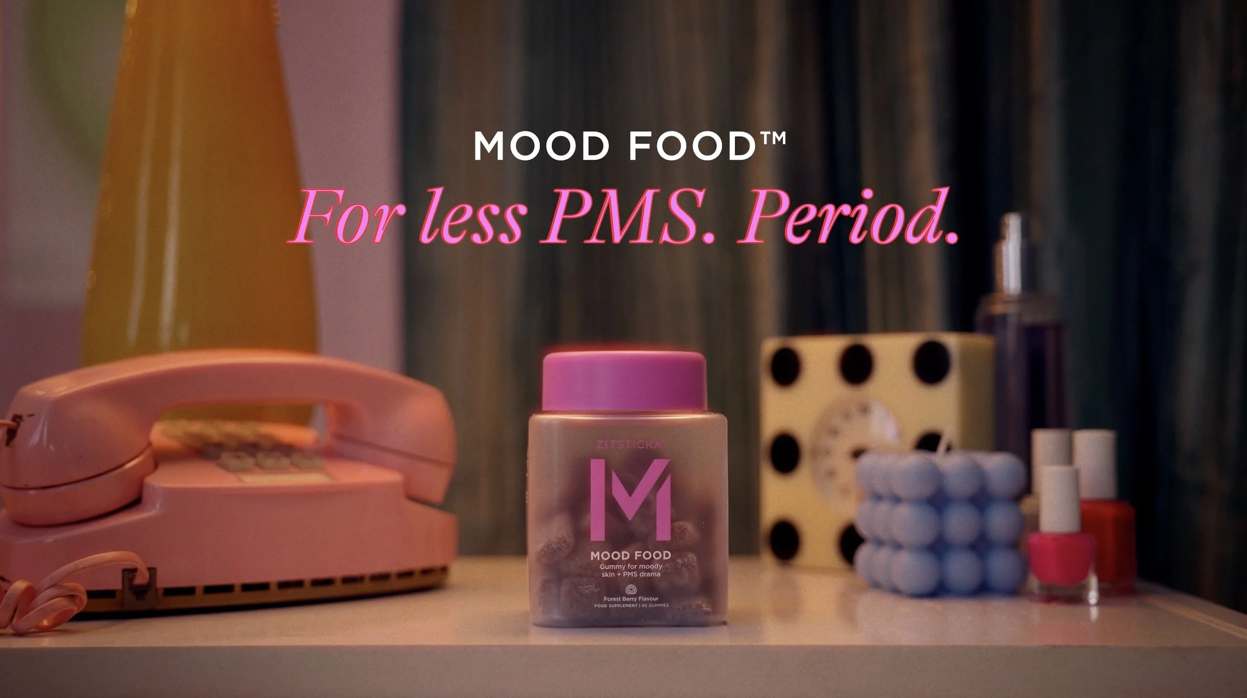 A pink rotary phone, a bottle of mood food gummy supplements, and various bottles and containers of medication and supplements on a desk or table.