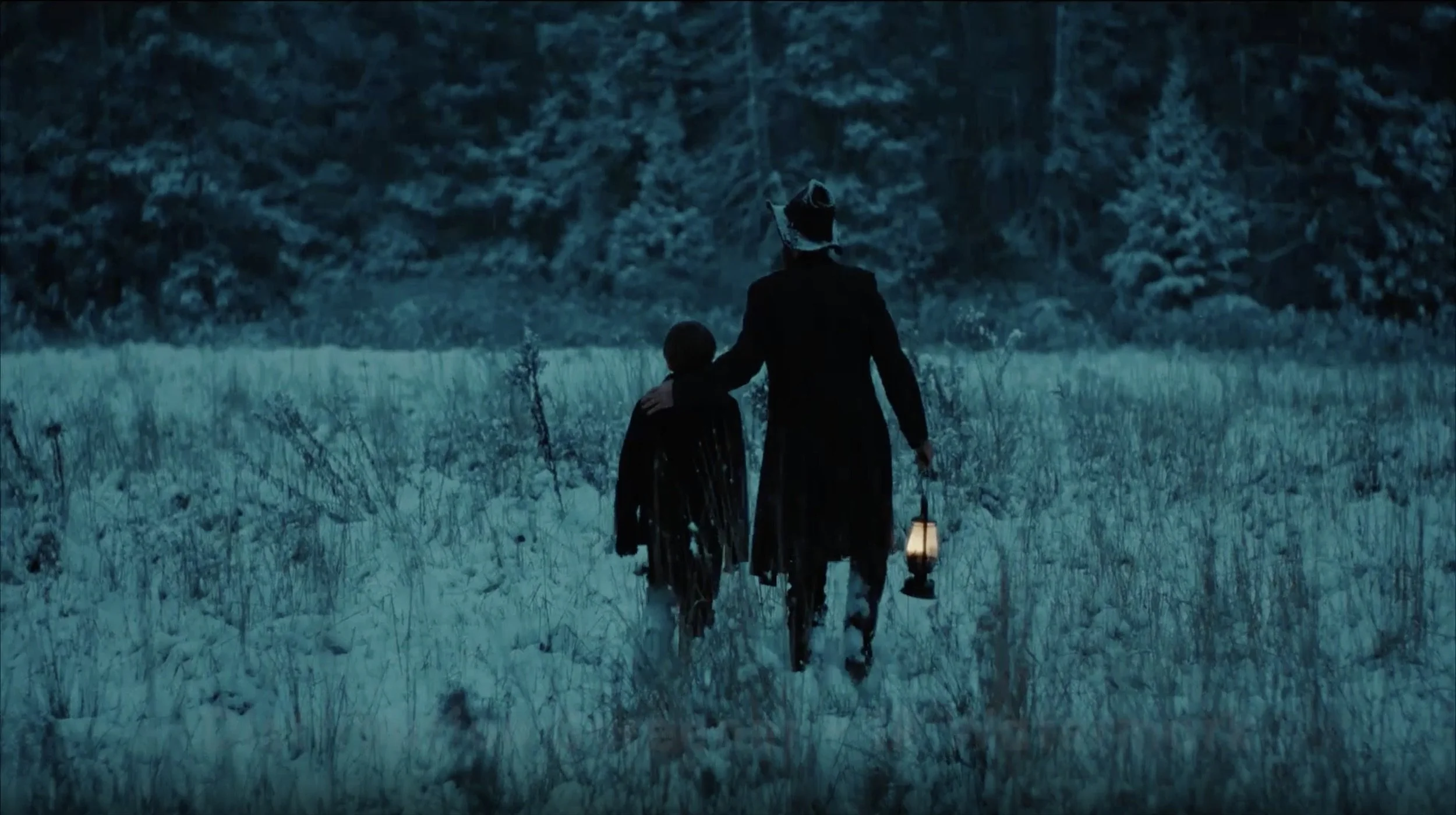 A person and a child walking through a grassy field at dusk, carrying lanterns, with a dense forest in the background.