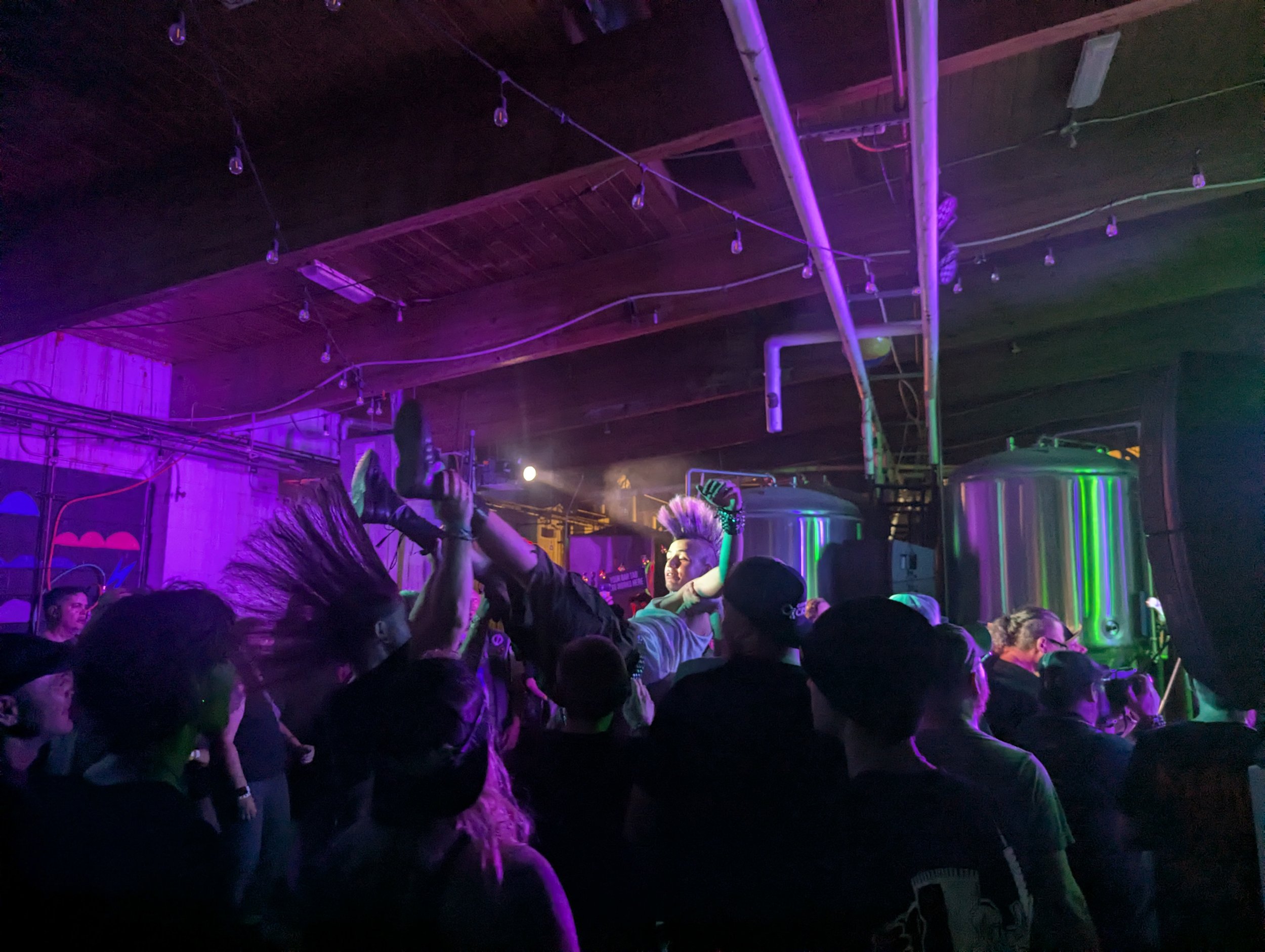 People dancing and enjoying music at an indoor concert or event with colorful lighting and a wooden ceiling.