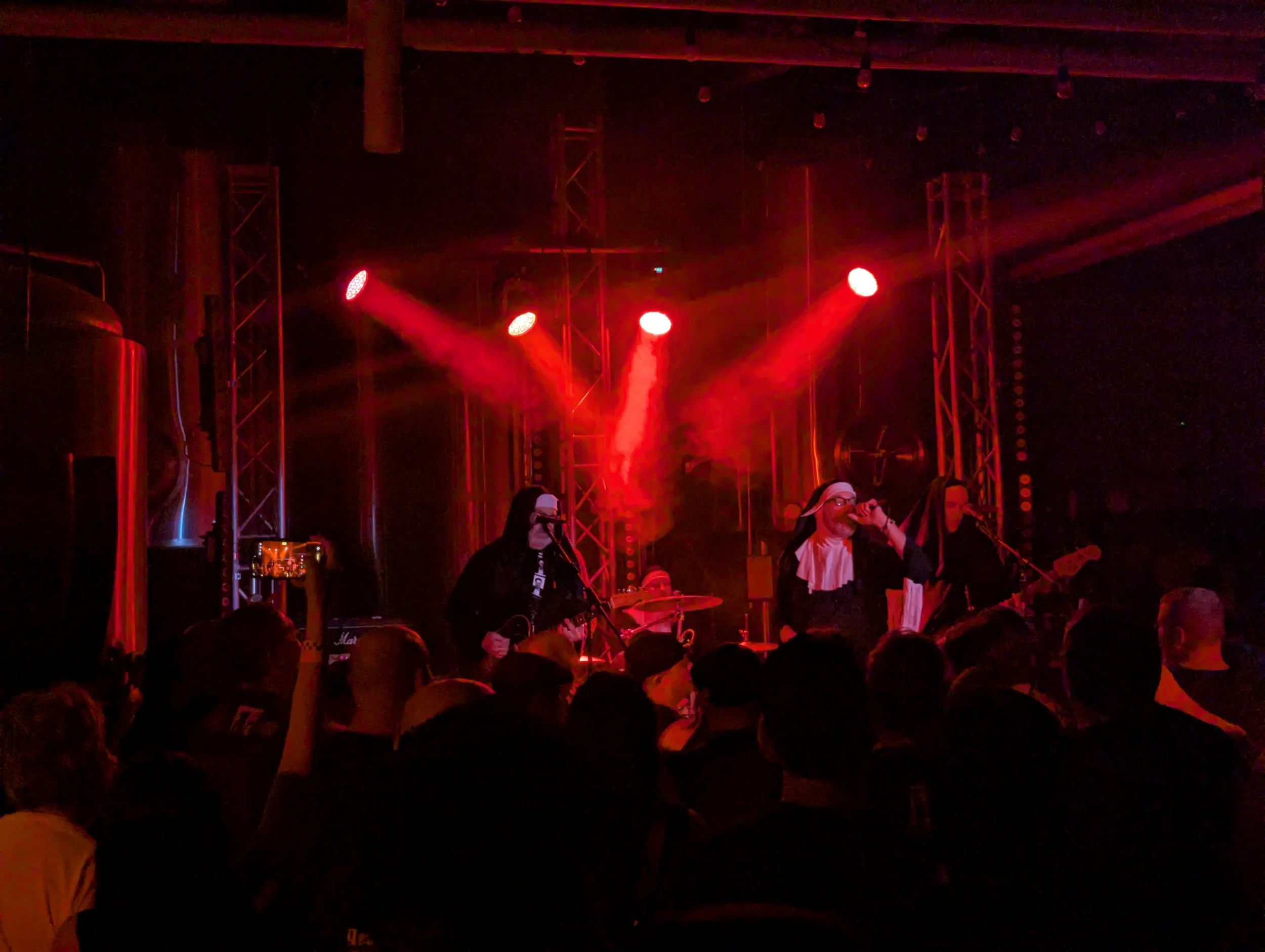 Concert scene with performers on stage illuminated by red lights and an audience in the foreground.