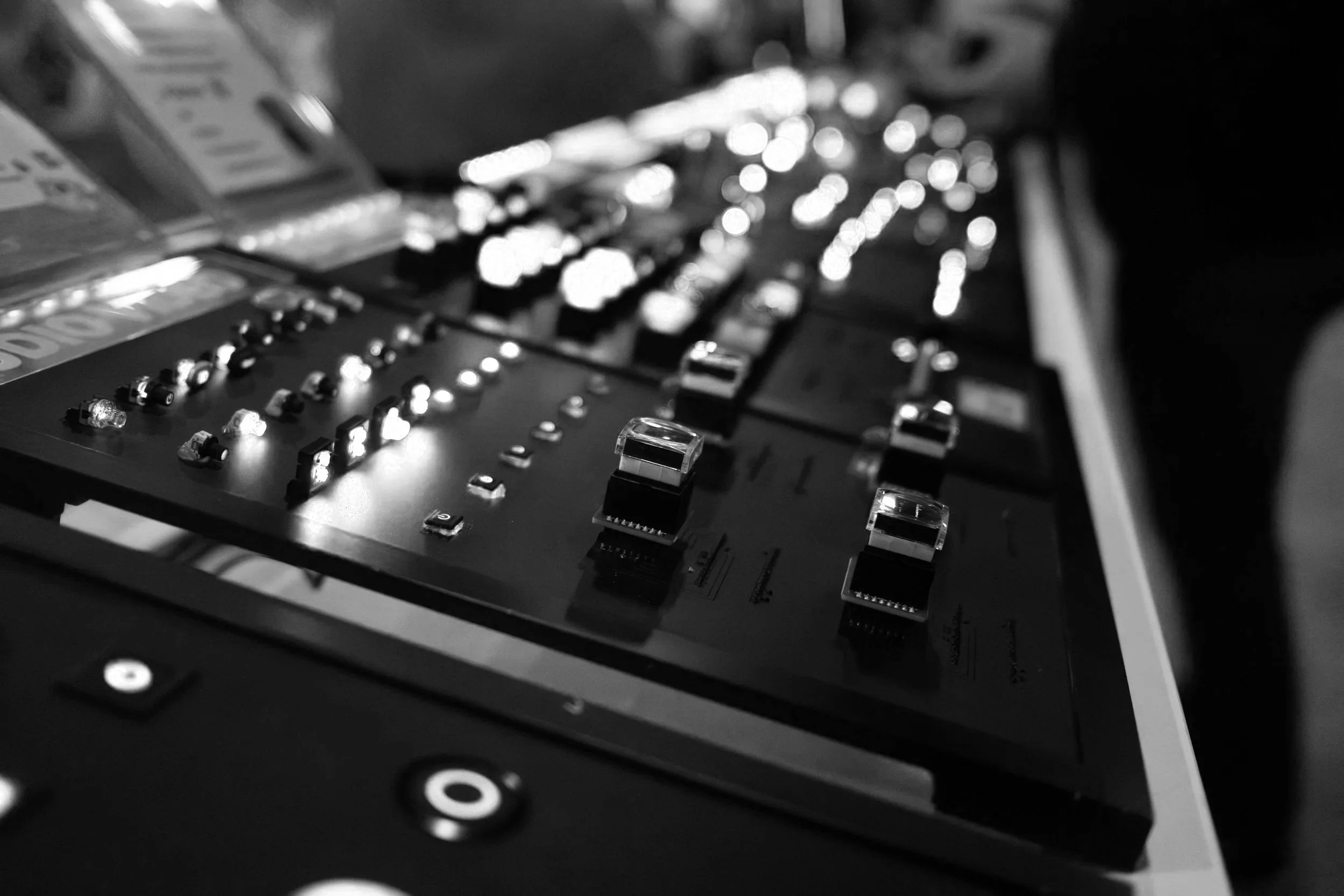 A close-up view of a DJ's turntable and mixer with various controls, knobs, and illuminated buttons in a black and white photograph.