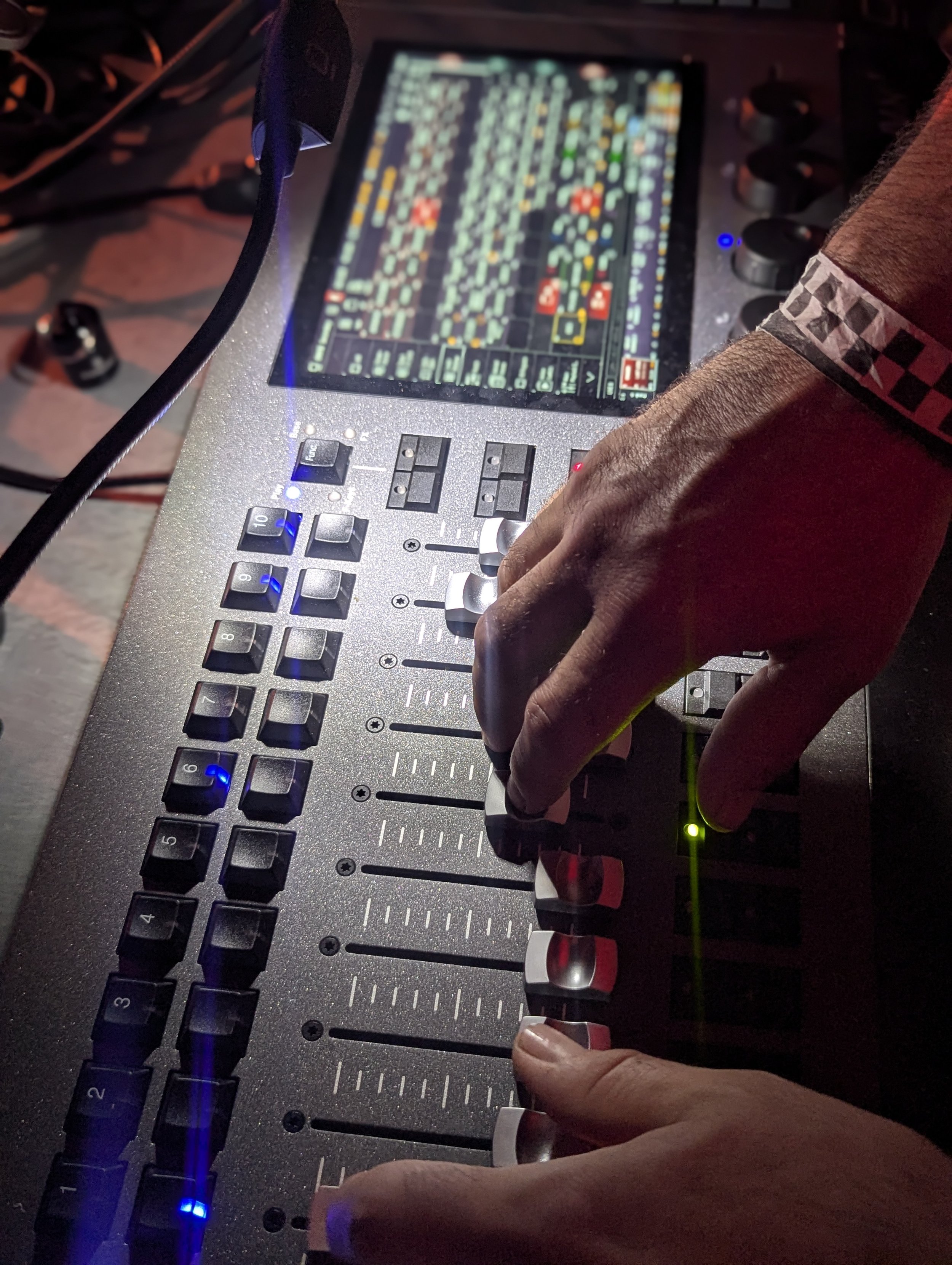 A DJ's hand is adjusting the knobs on a professional DJ mixer or controller, with a digital screen displaying colorful audio tracks and effects.