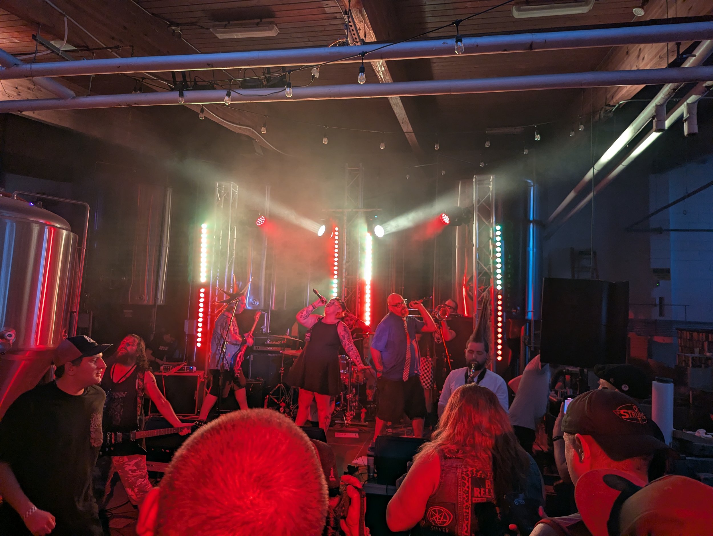 People enjoying a live music performance in a dimly lit venue with colorful stage lights, some people are dancing and socializing.