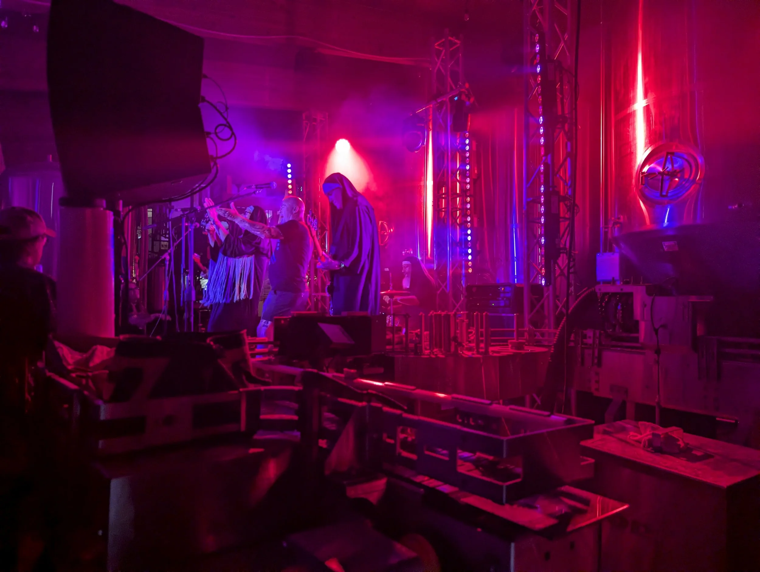 Stage with colorful purple and pink neon lights, people standing and performing, surrounded by equipment and scaffolding.