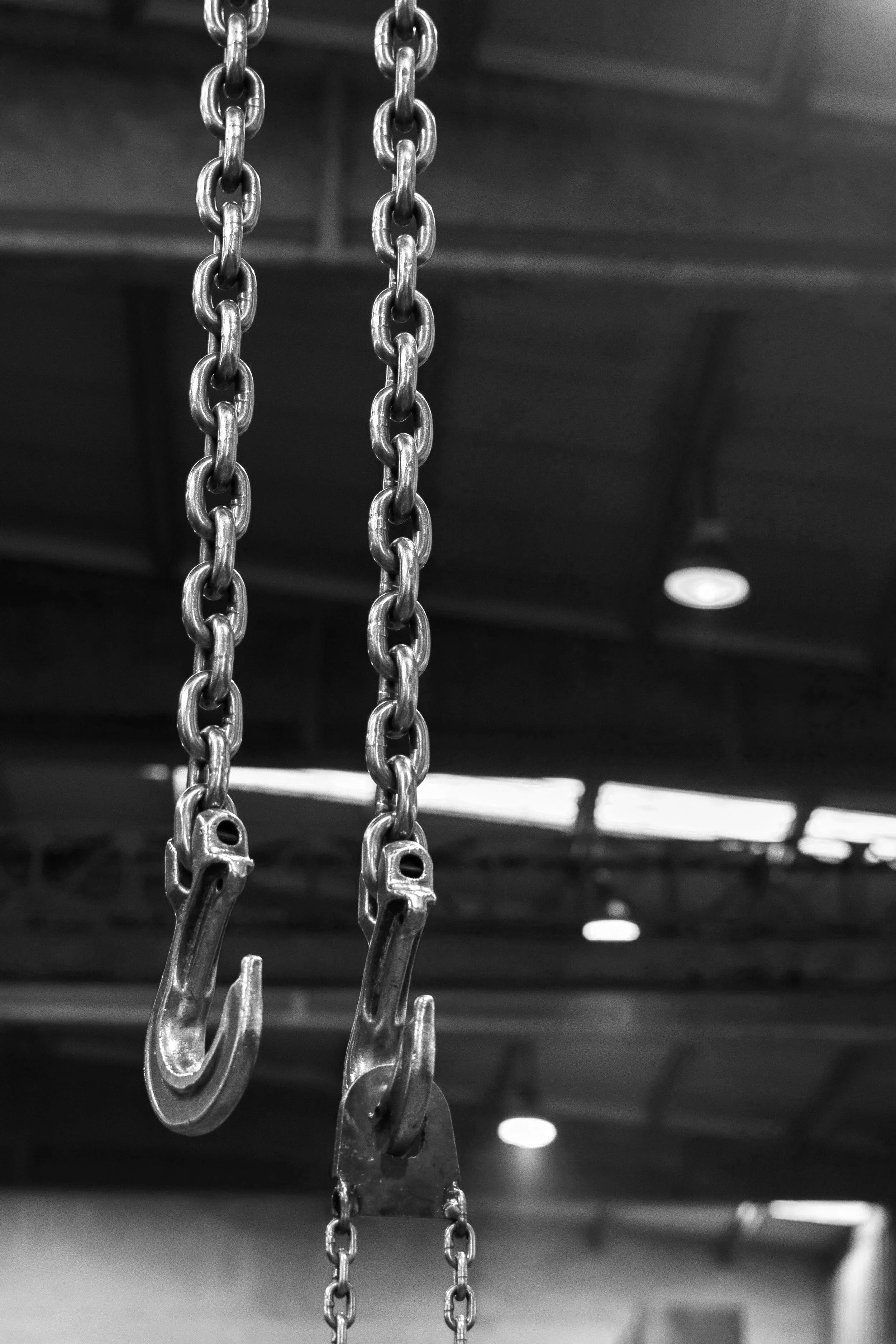 Close-up of metal hooks hanging from chains, with blurred ceiling and lights in the background.