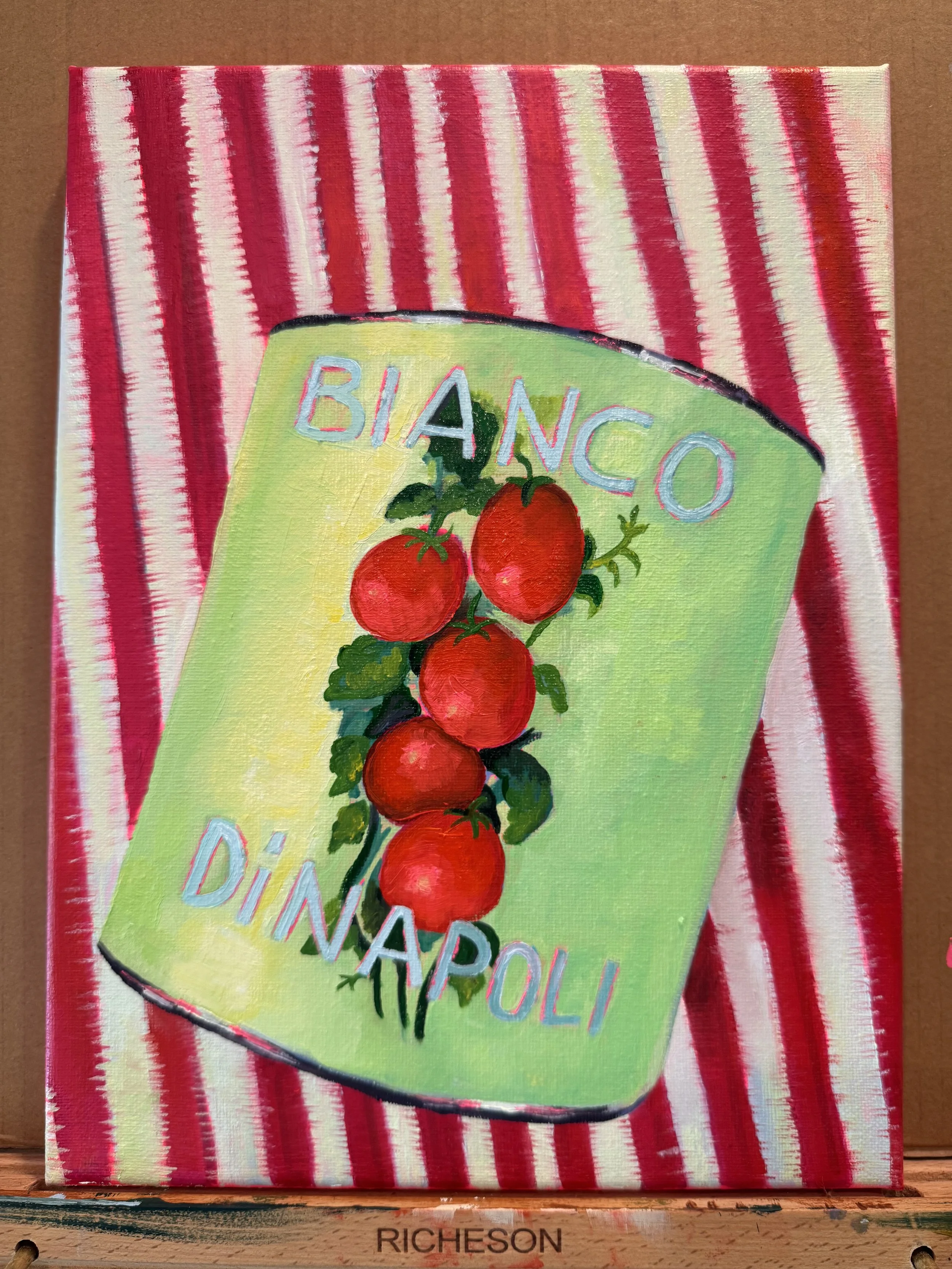 A colorful painting of a tomato plant on a package of Bianco Diavolo tomato seeds, with a background of red and white striped fabric.
