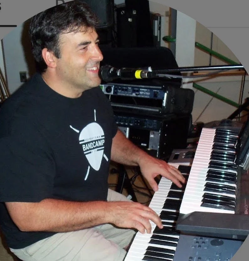 A man is playing a keyboard and singing into a microphone, smiling.