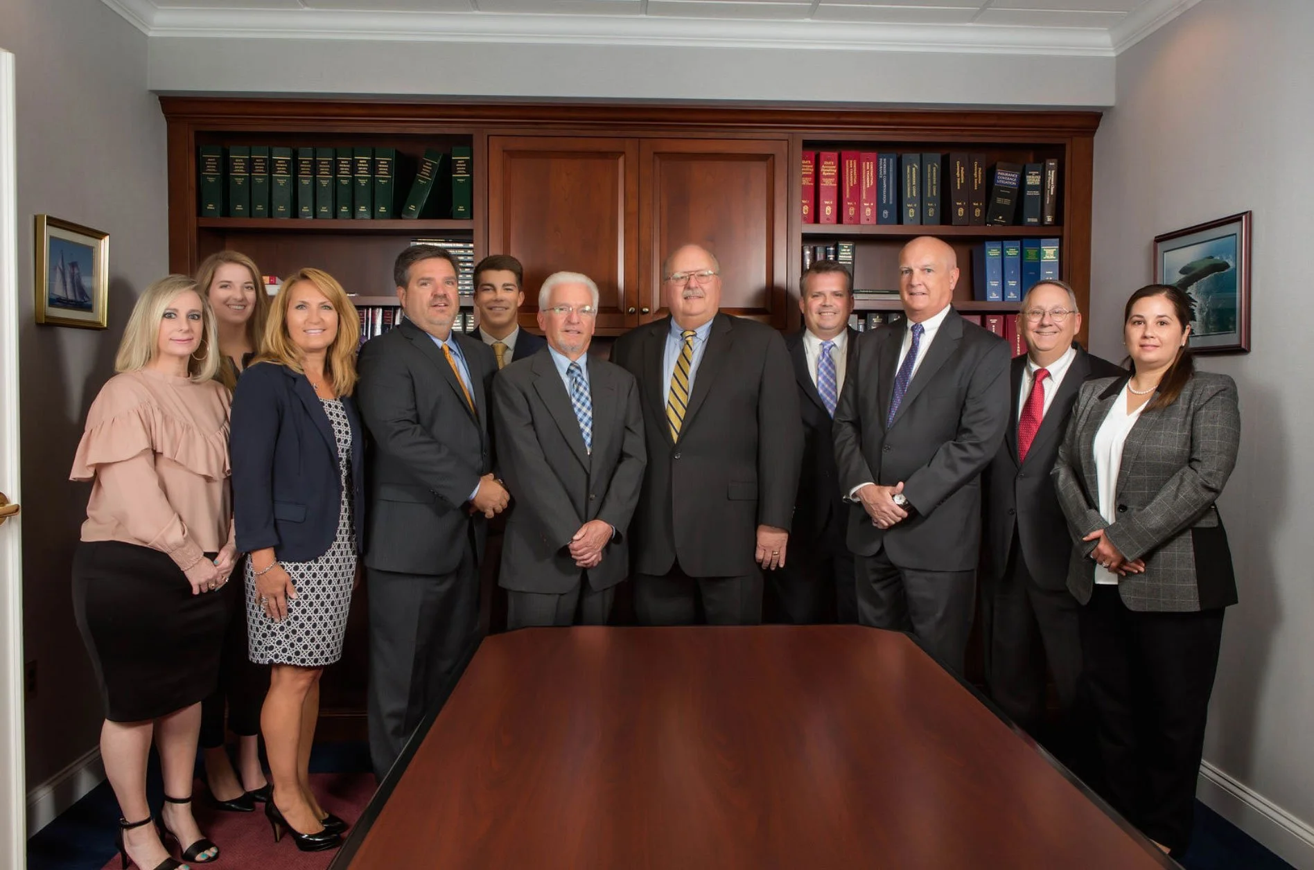 A group of ten professionally dressed people standing in a conference room behind a wooden table, smiling for a group photo.