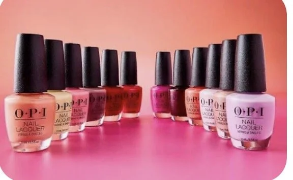 A collection of OPI nail polish bottles arranged in a curved line on a pink surface, with a gradient orange background.
