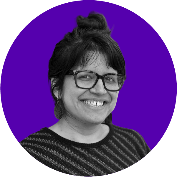 A woman with glasses and earrings smiling, with a black and white photo against a purple background.
