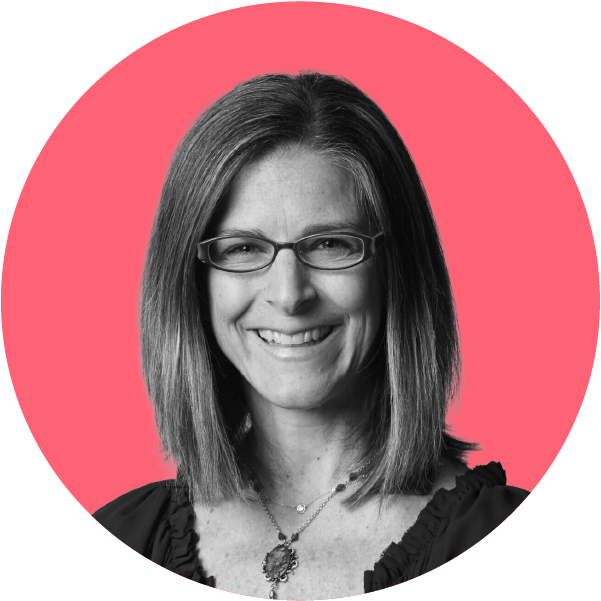 A woman with shoulder-length hair, glasses, and a necklace smiling in front of a pink and black background.