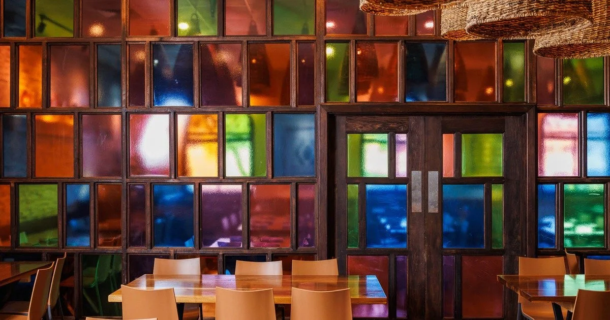 Interior of a colorful restaurant with stained glass windows and wooden tables and chairs.