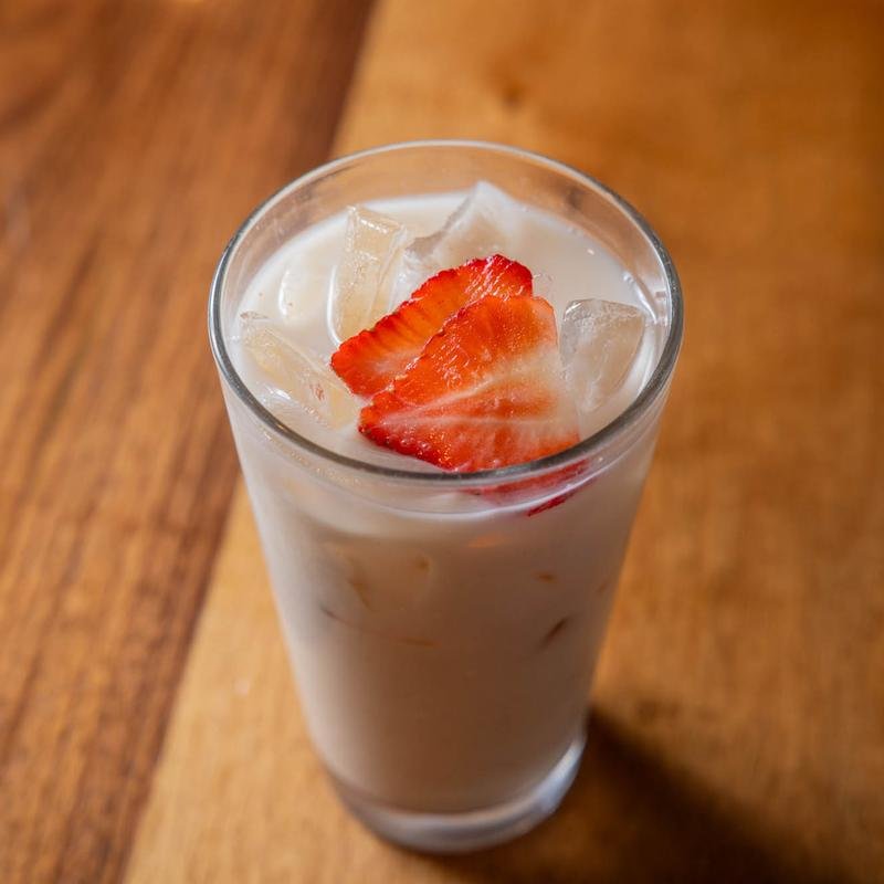 A tall glass of strawberry milk with ice and sliced strawberries on top, on a wooden table.