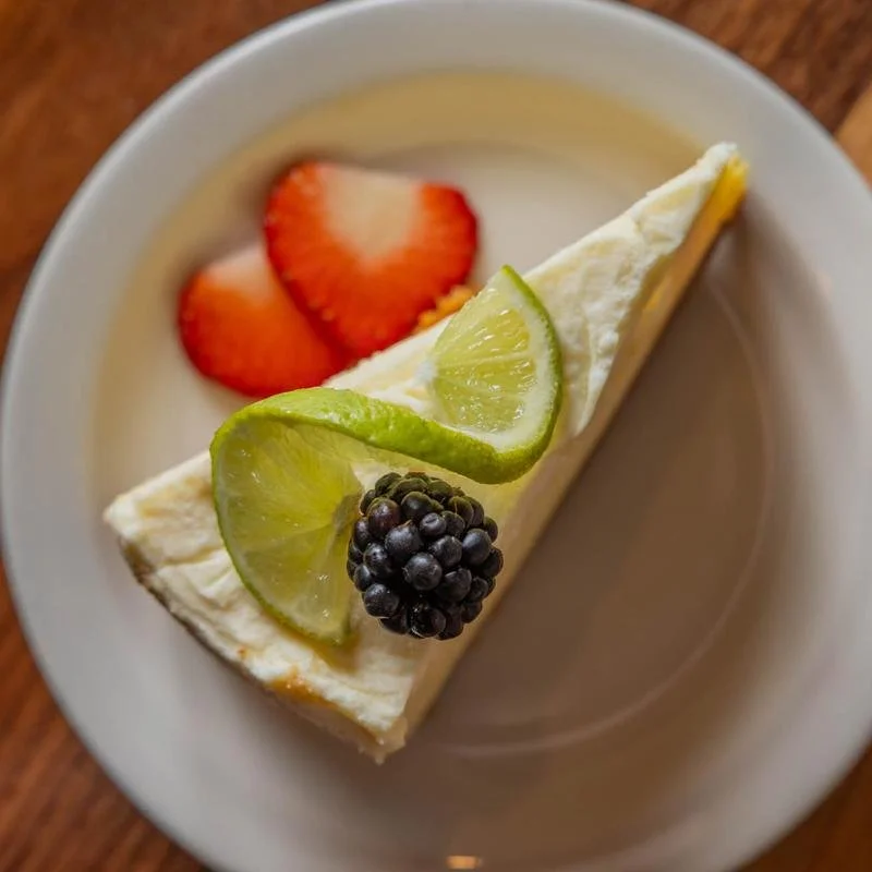 Slice of key lime pie garnished with lime, blackberry, and strawberries on a white plate.