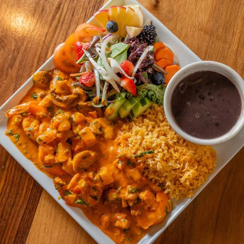 A plate of Mexican food with rice, a shrimp and vegetable stew, a side salad, and a cup of black beans.