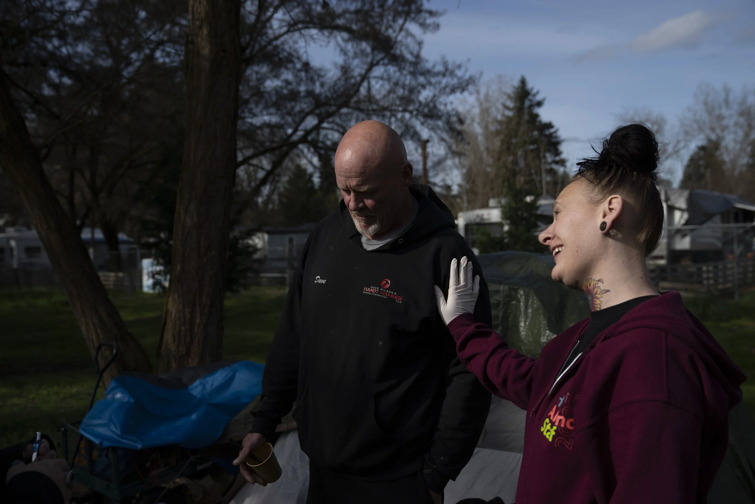 A volunteer checks in with David Wilson near his tent in Riverside Park on Thursday, March 21, 2024, in Grants Pass, Ore. Wilson was among those getting free food and breakfast brought by volunteers to the park that morning. 