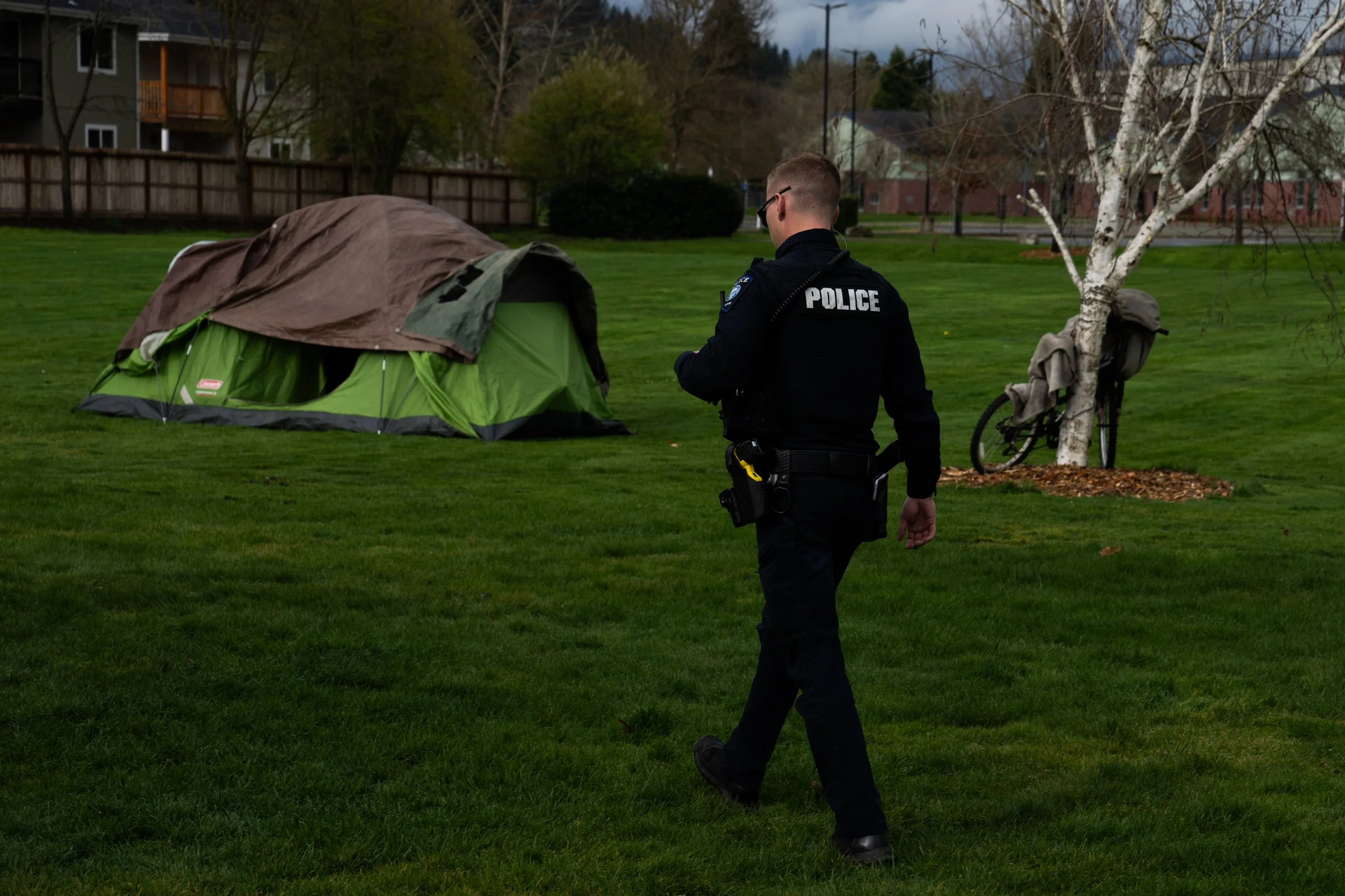 With Fruitdale Elementary School in the background, a Grants Pass police officer walks to check on a homeless person after relatives asked for a welfare check at Fruitdale Park on Saturday, March 23, 2024, in Grants Pass, Ore. 