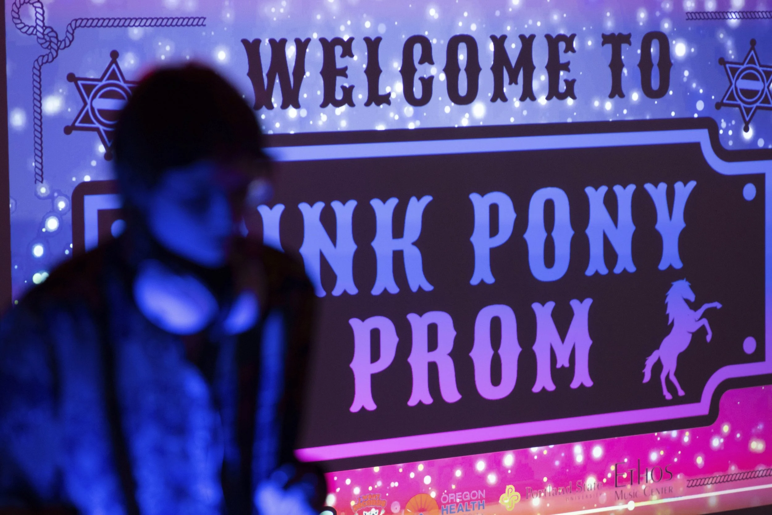 A DJ is seen in front of a sign for a “Pink Pony Prom” organized by the Sexual & Gender Minority Youth Resource Center, part of New Avenues for Youth, a nonprofit dedicated to ending youth homelessness, on Friday, May 30, 2025, in Portland, Ore. 