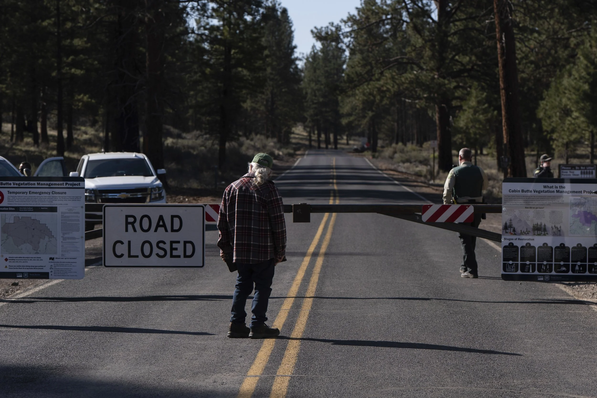 A person looks out at a road closure along China Hat Road as U.S. Forest Service officials are seen behind the barrier that leads to a homeless encampment in Deschutes National Forest, Thursday, May 1, 2025, near Bend, Ore. 