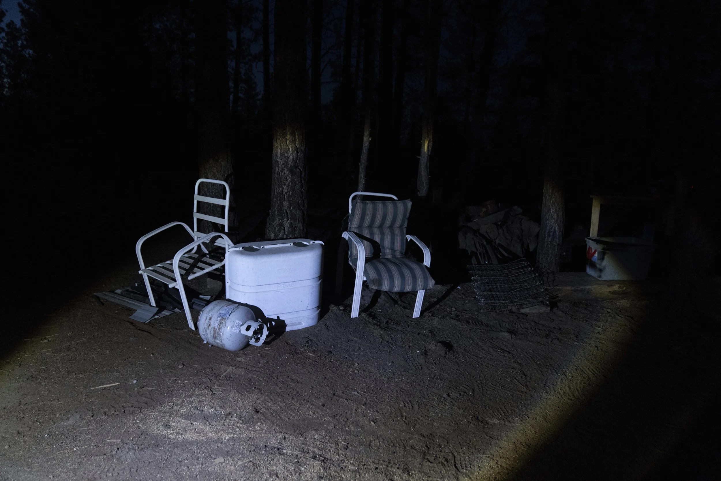 A flashlight from Mandy Bryant’s shines on chairs propped up by trees at a homeless encampment in Deschutes National Forest Wednesday, April 30, 2025 near Bend, Ore. 