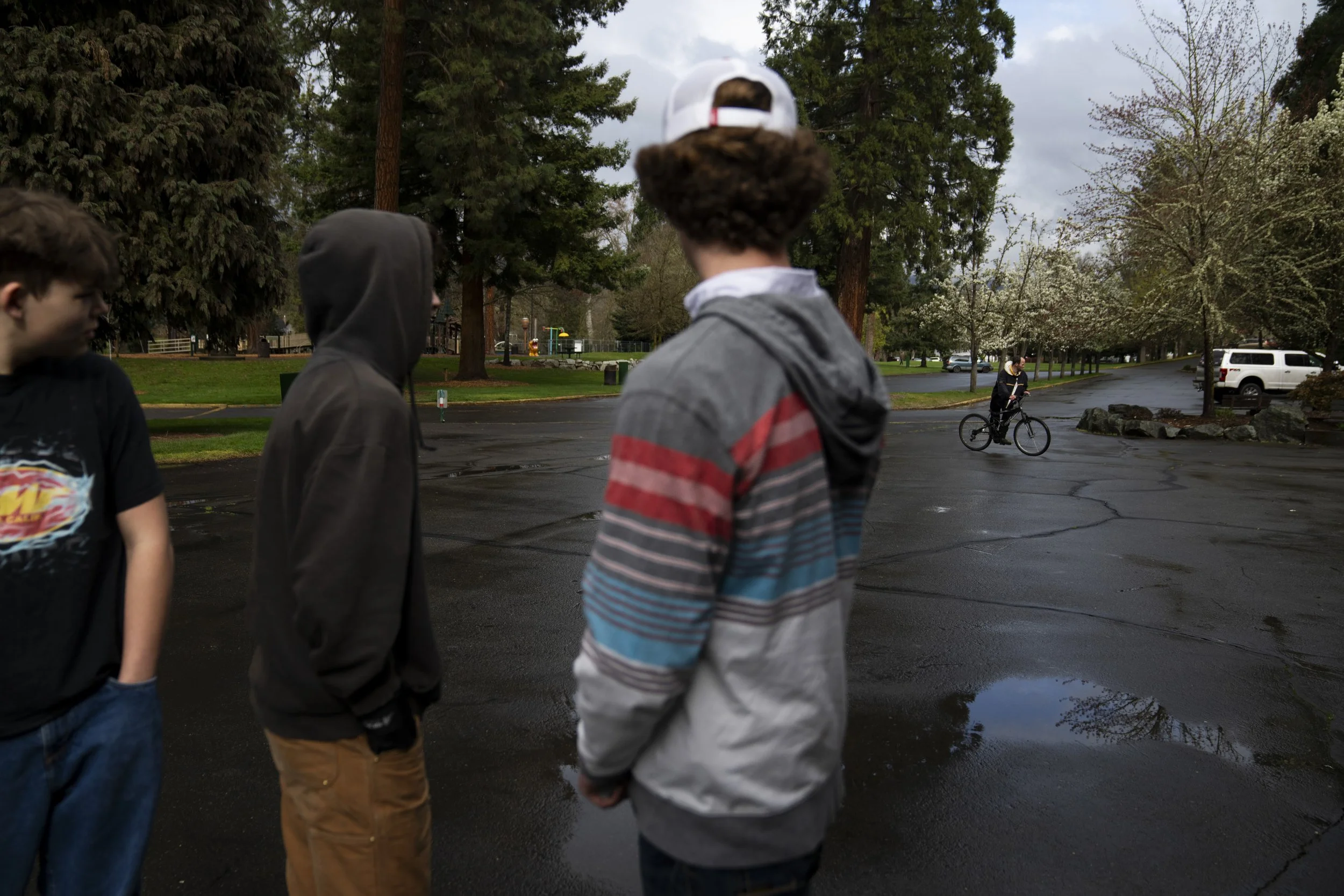 A group of teenagers watch as a homeless person rides a bike past them in Riverside Park, Friday, March 22, 2024, in Grants Pass, Ore. 