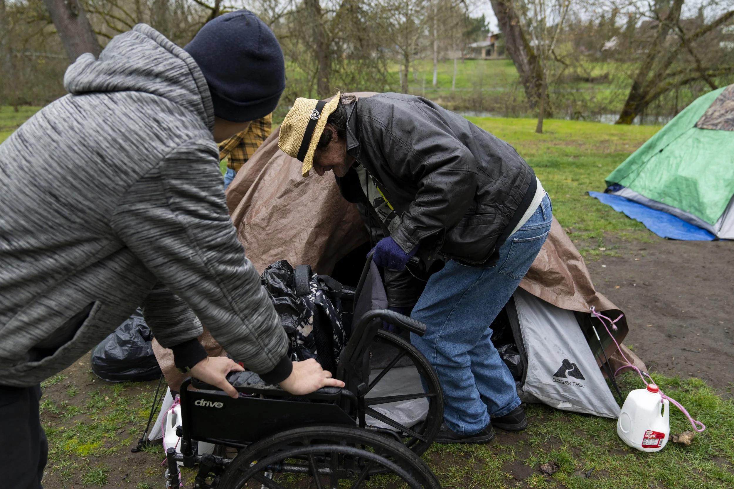 A volunteer holds on to a wheelchair as they help Trevellian "Max" Hartfelt get into his tent after relocation on Saturday, March 23, 2024, in Grants Pass, Ore. 
