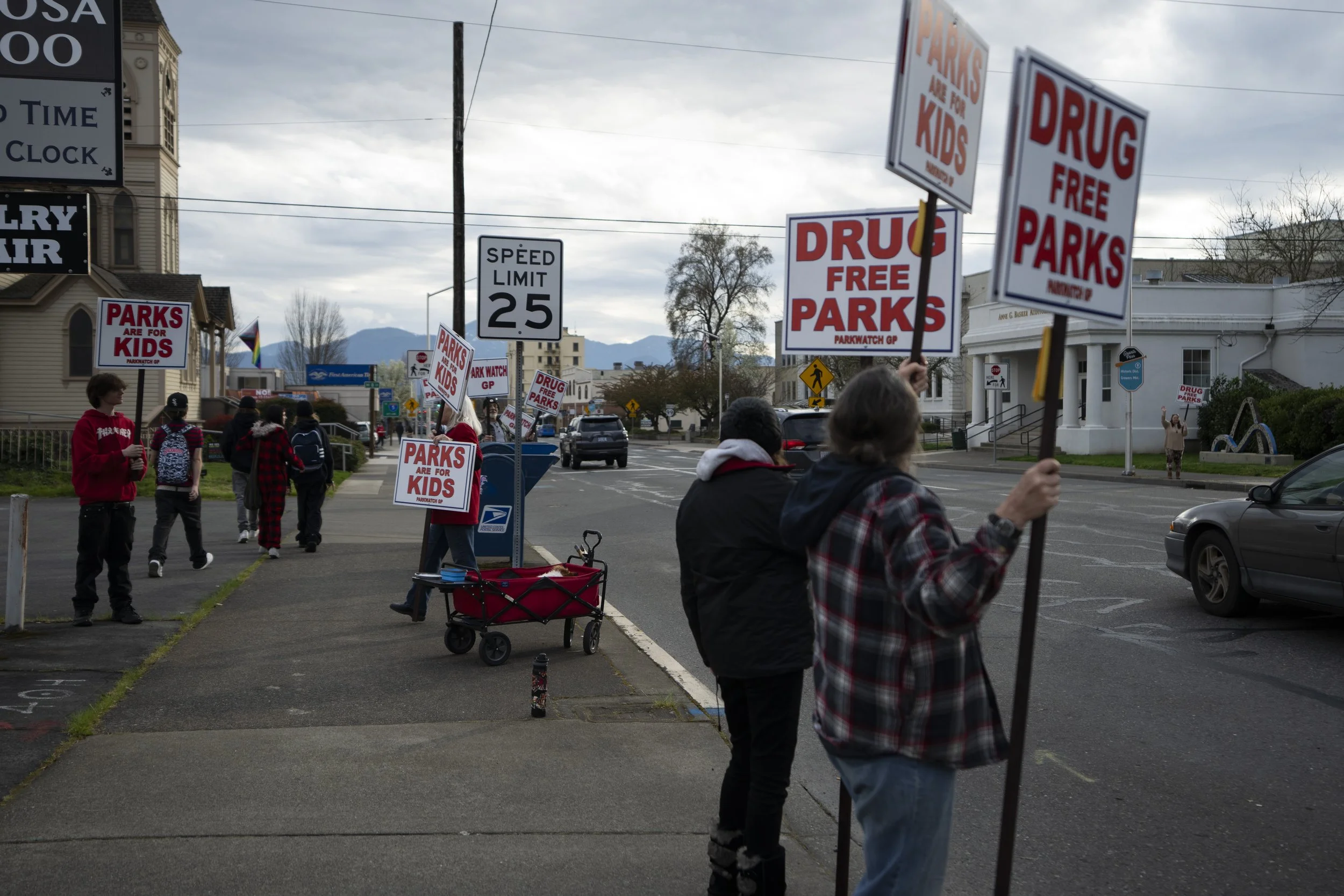 A teenager who was walking by stops to hold a sign as a member of the self-proclaimed “park watch” group walks to speak with them outside City Hall on Wednesday, March 20, 2024, in Grants Pass, Ore.