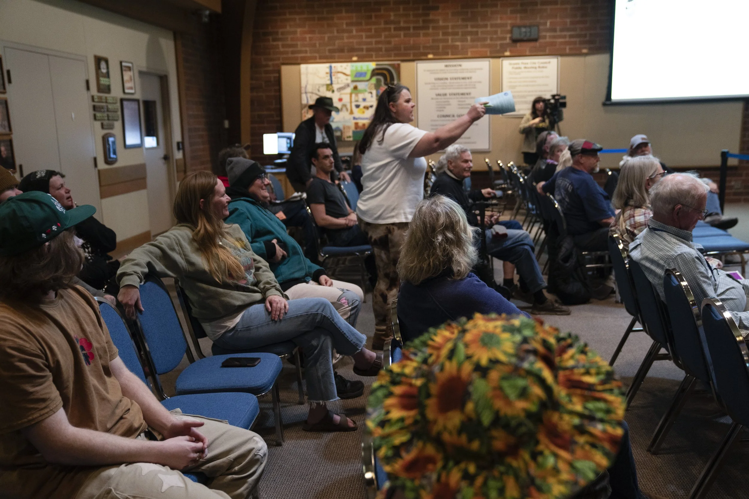 Cassy Leach, seated second from left next to two empty seats, watches community members react in a City Council meeting to questions about whether public comment would be heard after a veto by Grants Pass Mayor Sara Bristol on Wednesday, March 20, 20