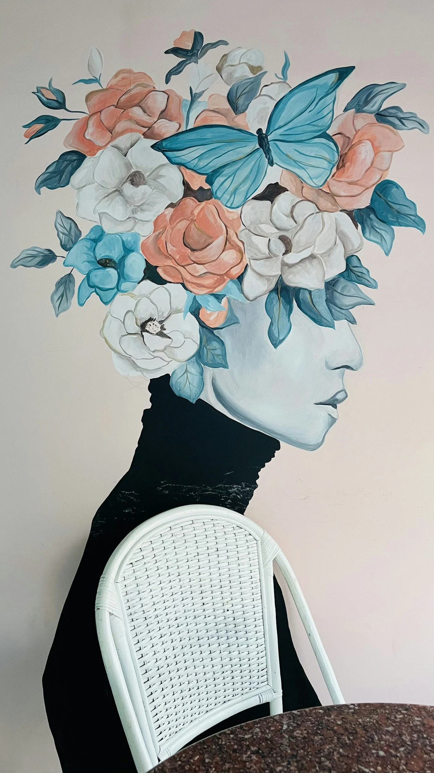 Wall mural of a woman's face in profile with her hair composed of large pastel-colored flowers and a blue butterfly.
