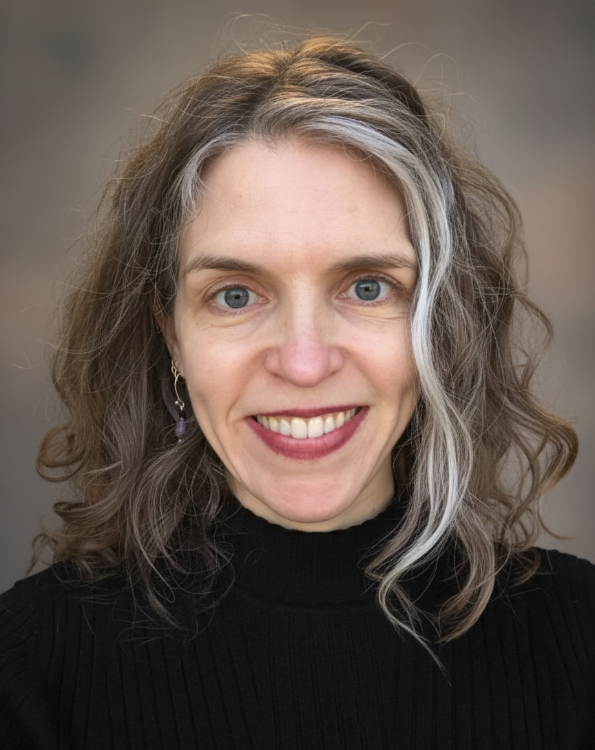A woman with shoulder-length wavy hair with a streak of white, wearing a black turtleneck, smiling at the camera.